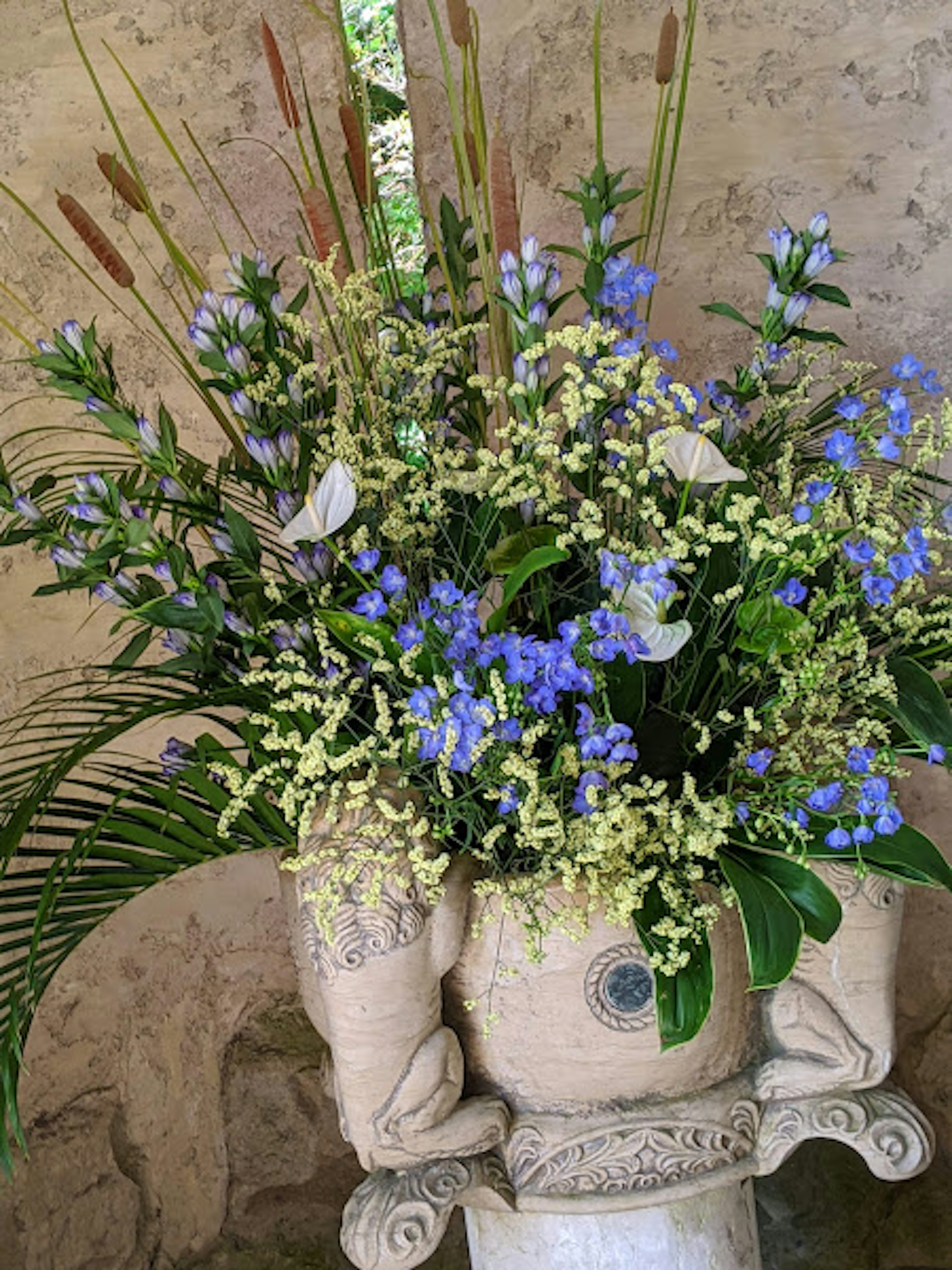 Blumenarrangement mit blauen Blumen und grünen Blättern in einer dekorativen Vase