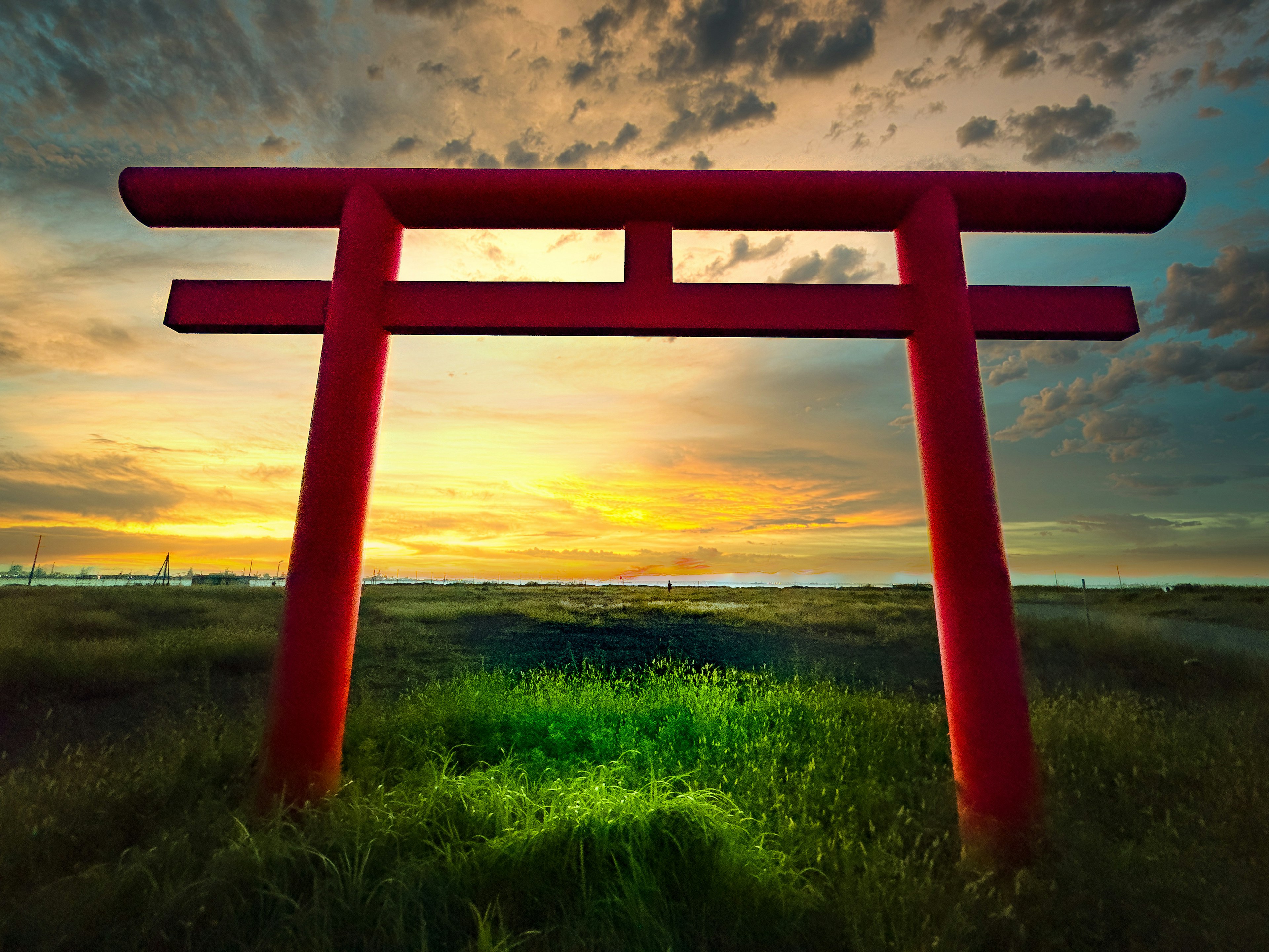 夕日の前に立つ赤い鳥居と緑の草原