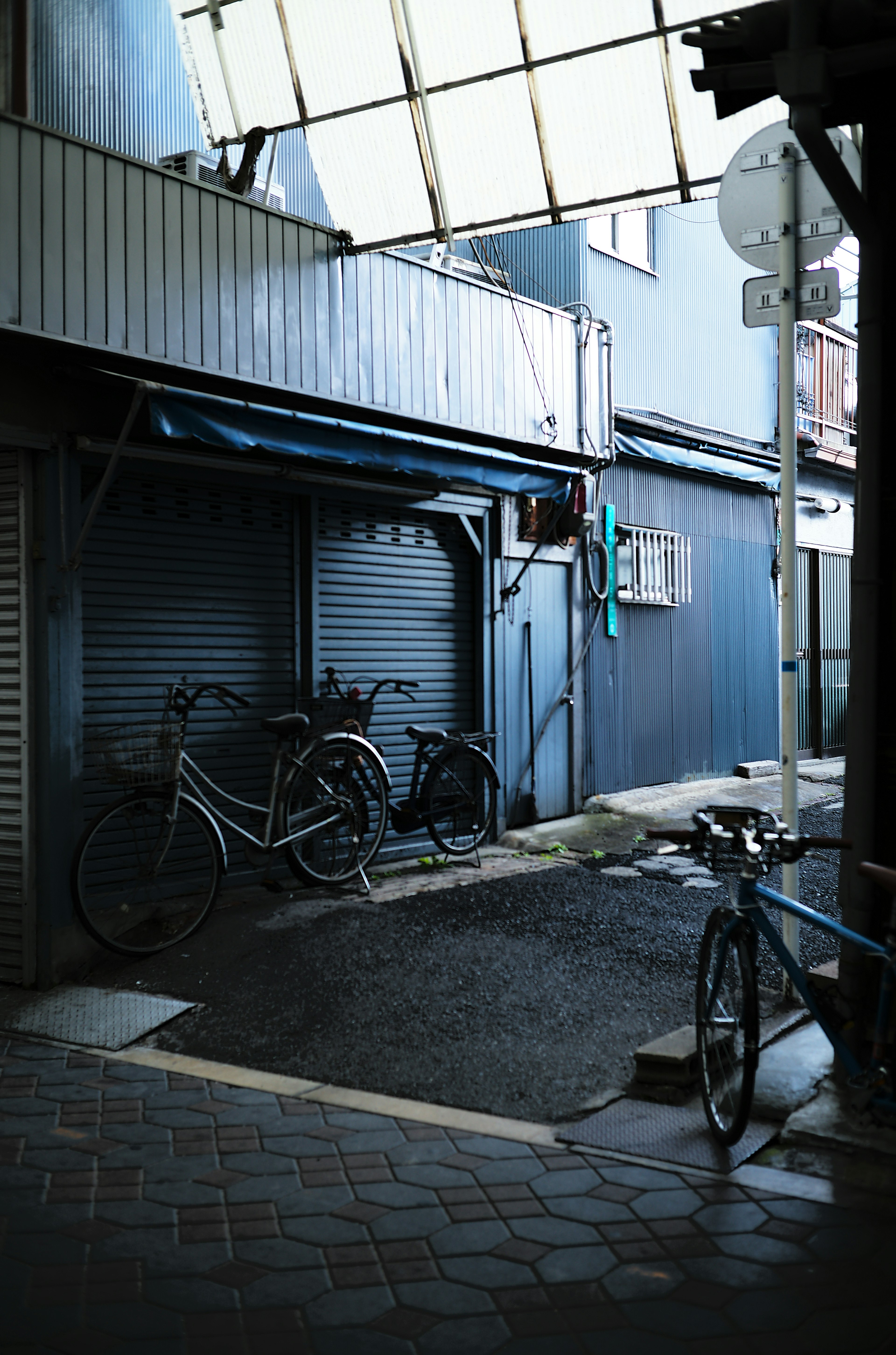 Bicycles parked in a narrow alley with blue walls and a shuttered storefront