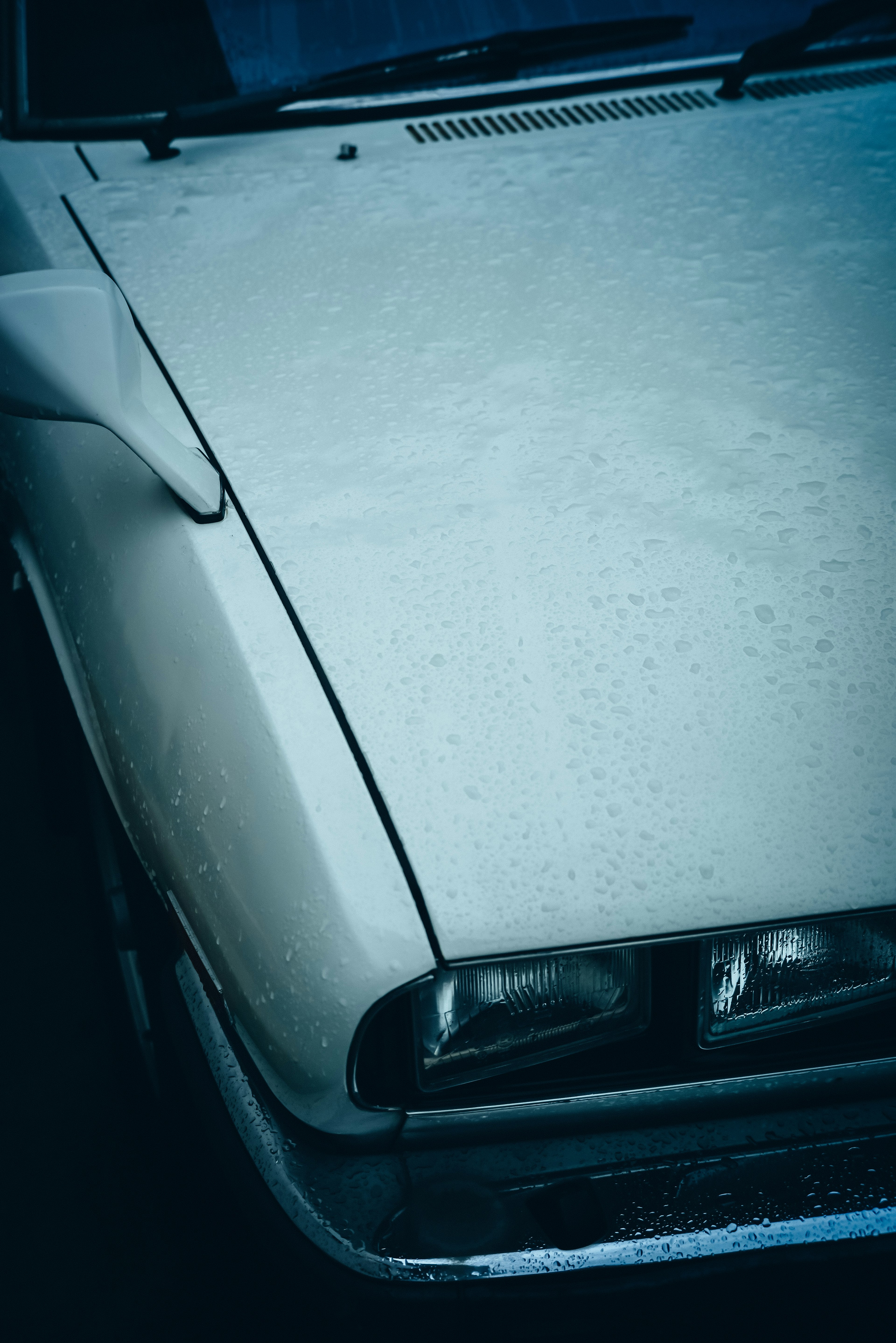 Primer plano del capó y los faros de un coche blanco mojado