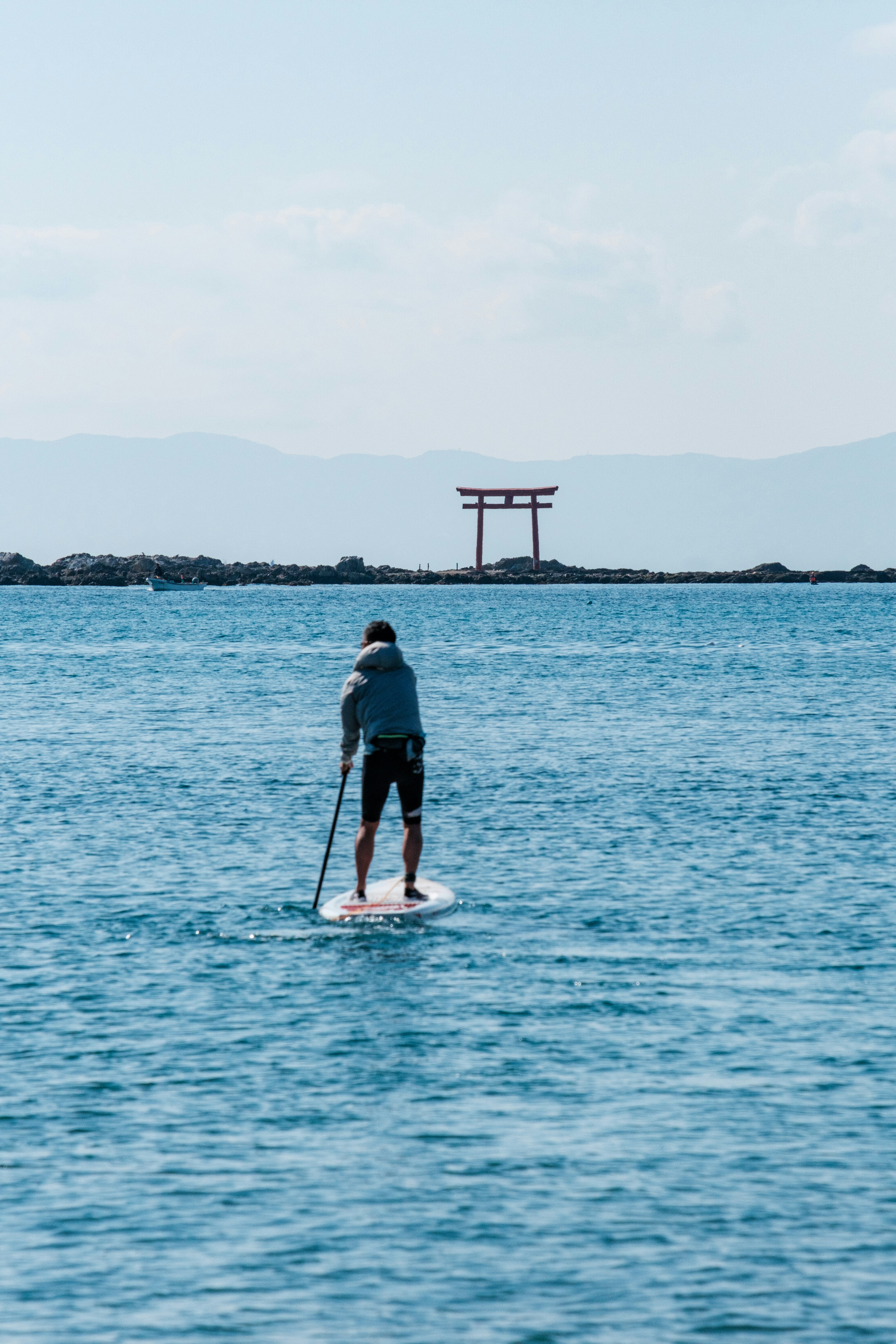 Persona che fa paddleboarding nell'oceano con un torii sullo sfondo