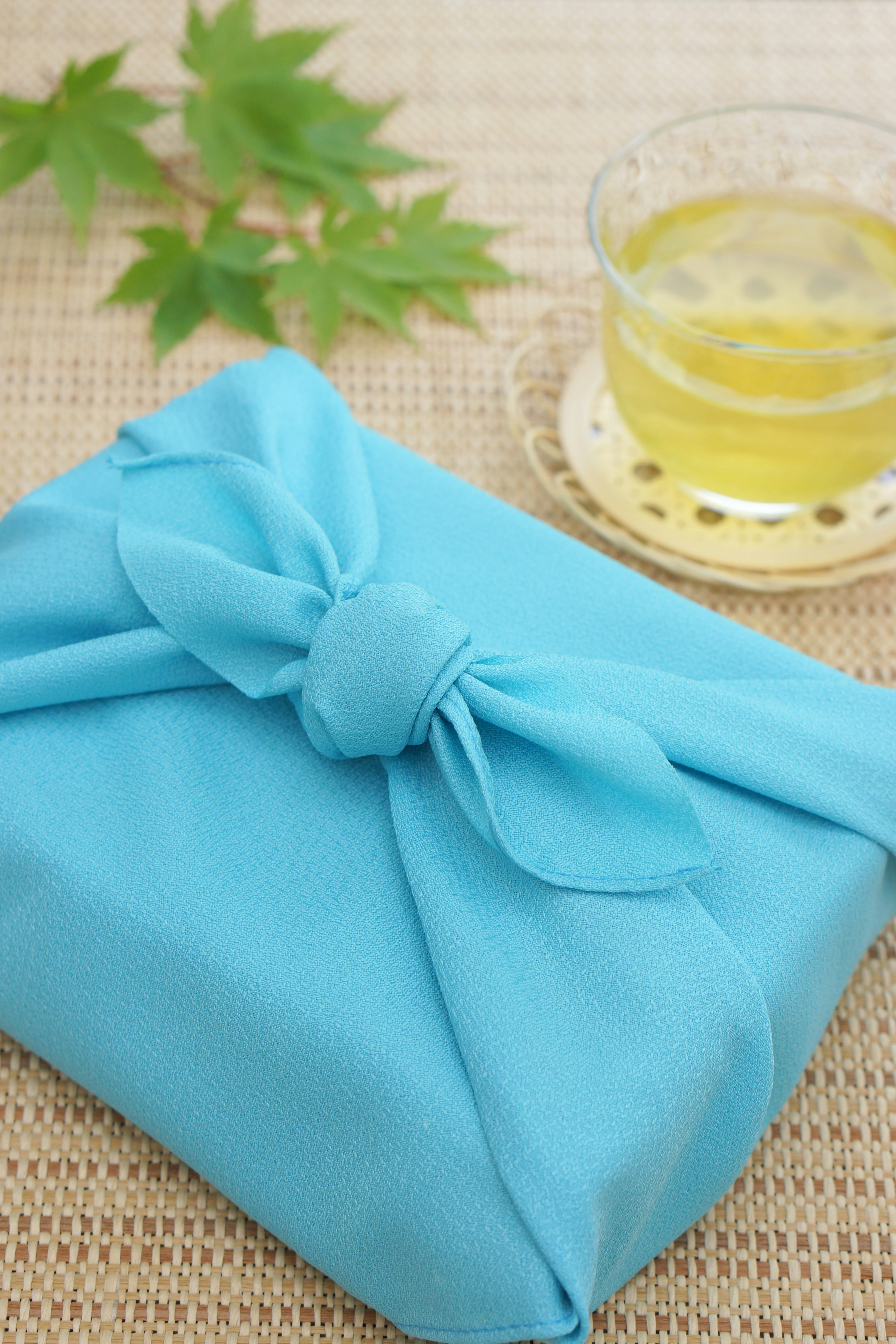 Blue wrapped gift with a bow and green leaves beside a cup of tea