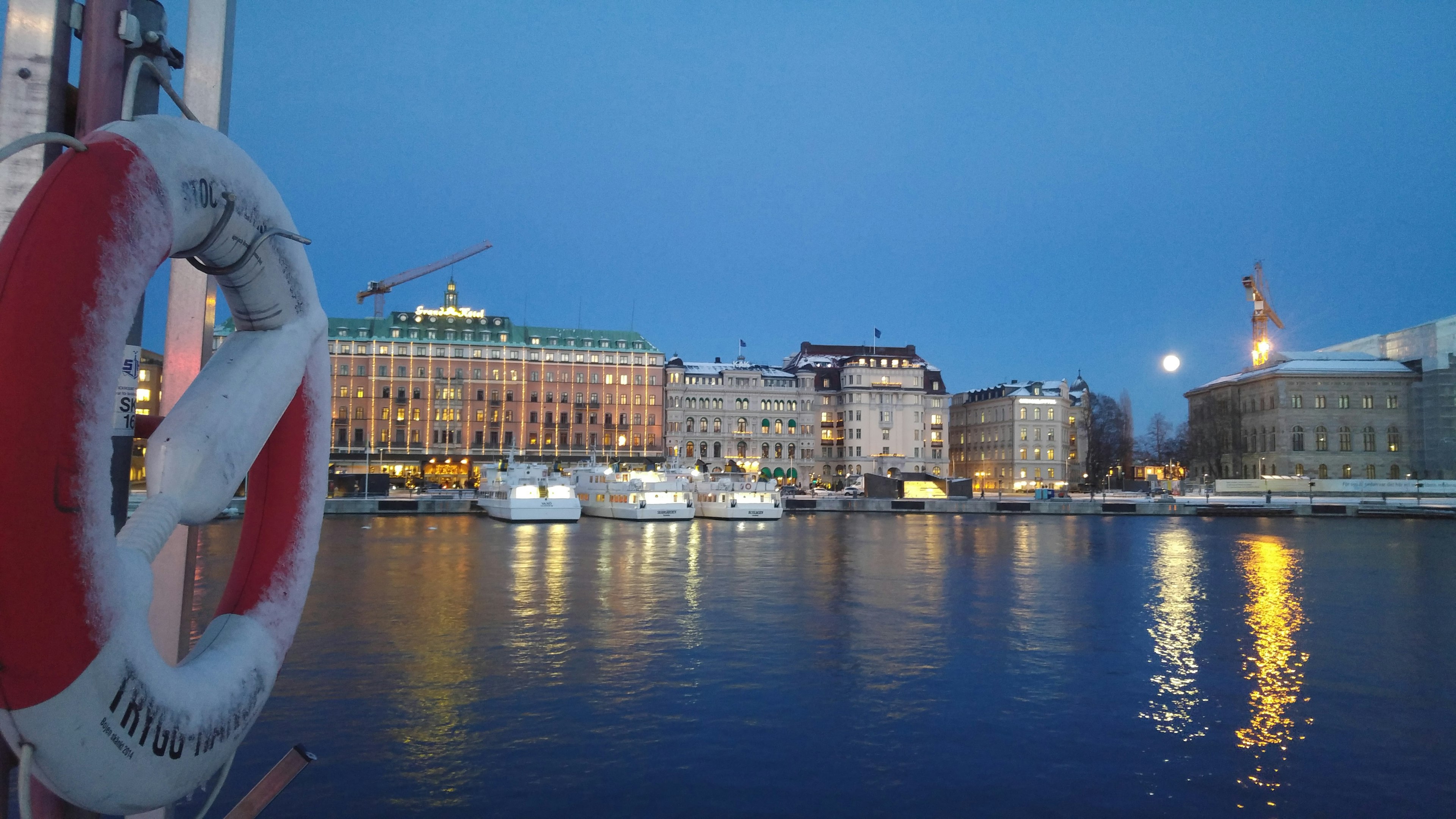 Abendliche Szene mit Gebäuden, die sich im Wasser spiegeln und einem Rettungsring