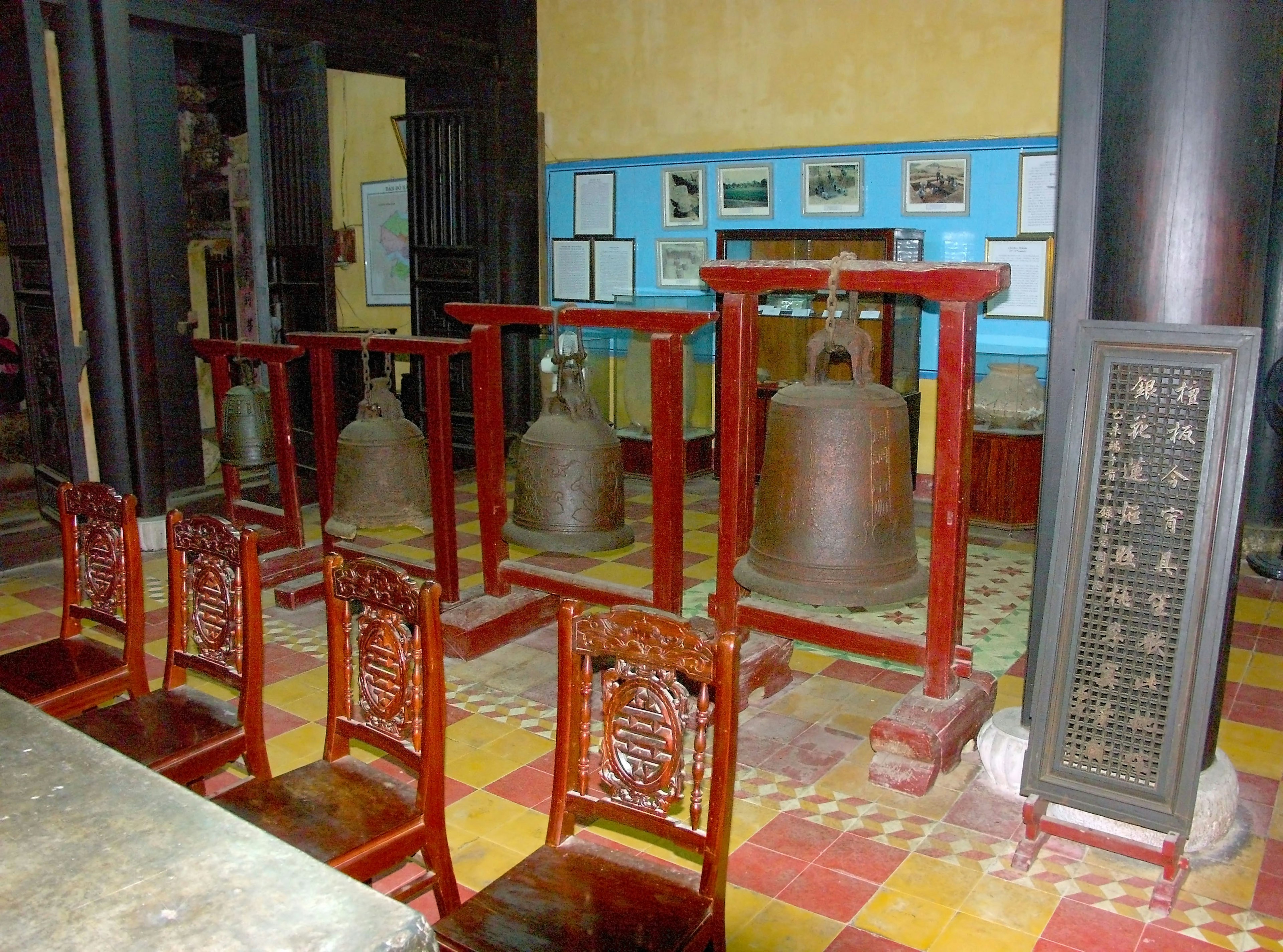 A serene space featuring bells arranged in a temple with wooden chairs