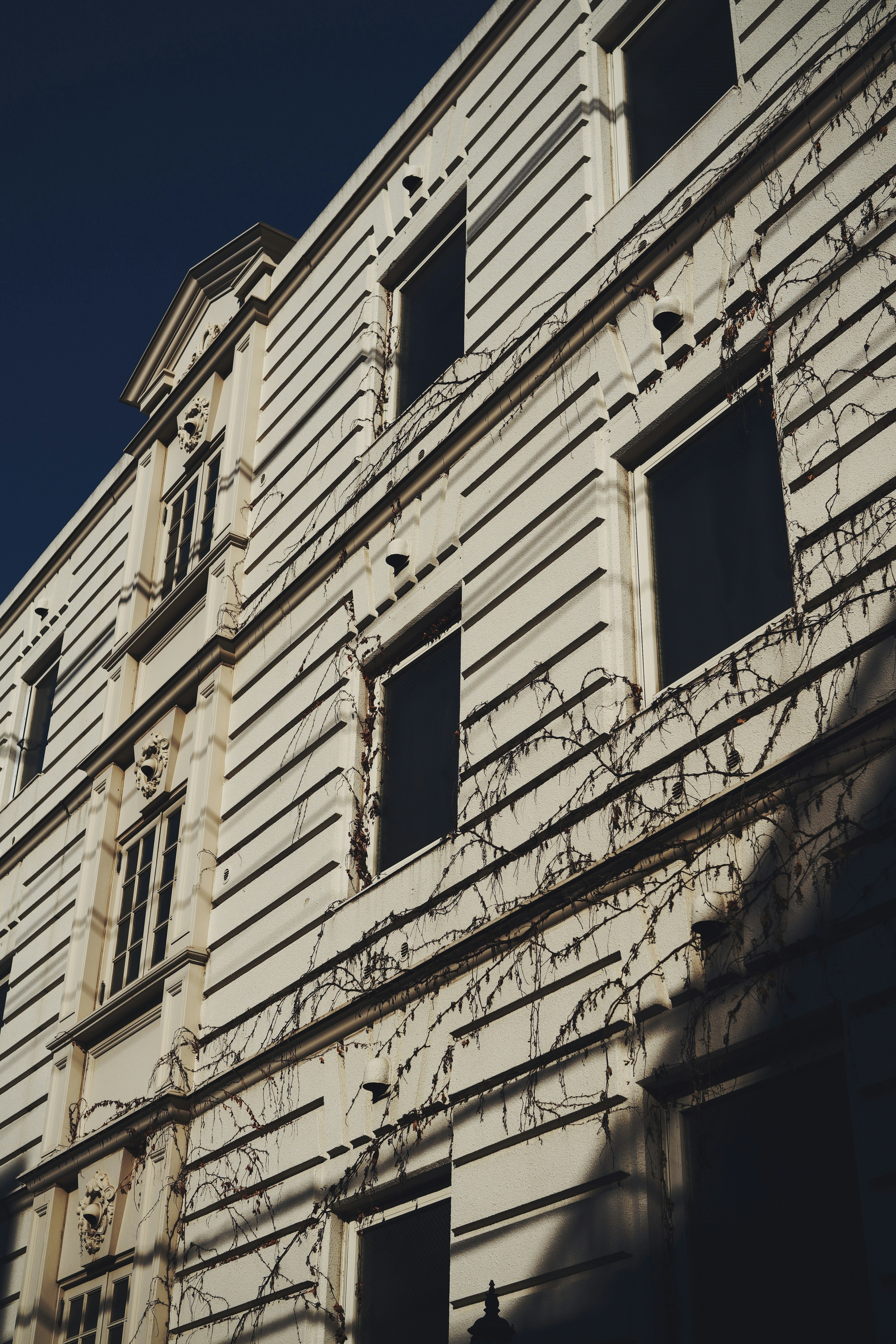 A historic building with a white facade and multiple windows casting shadows