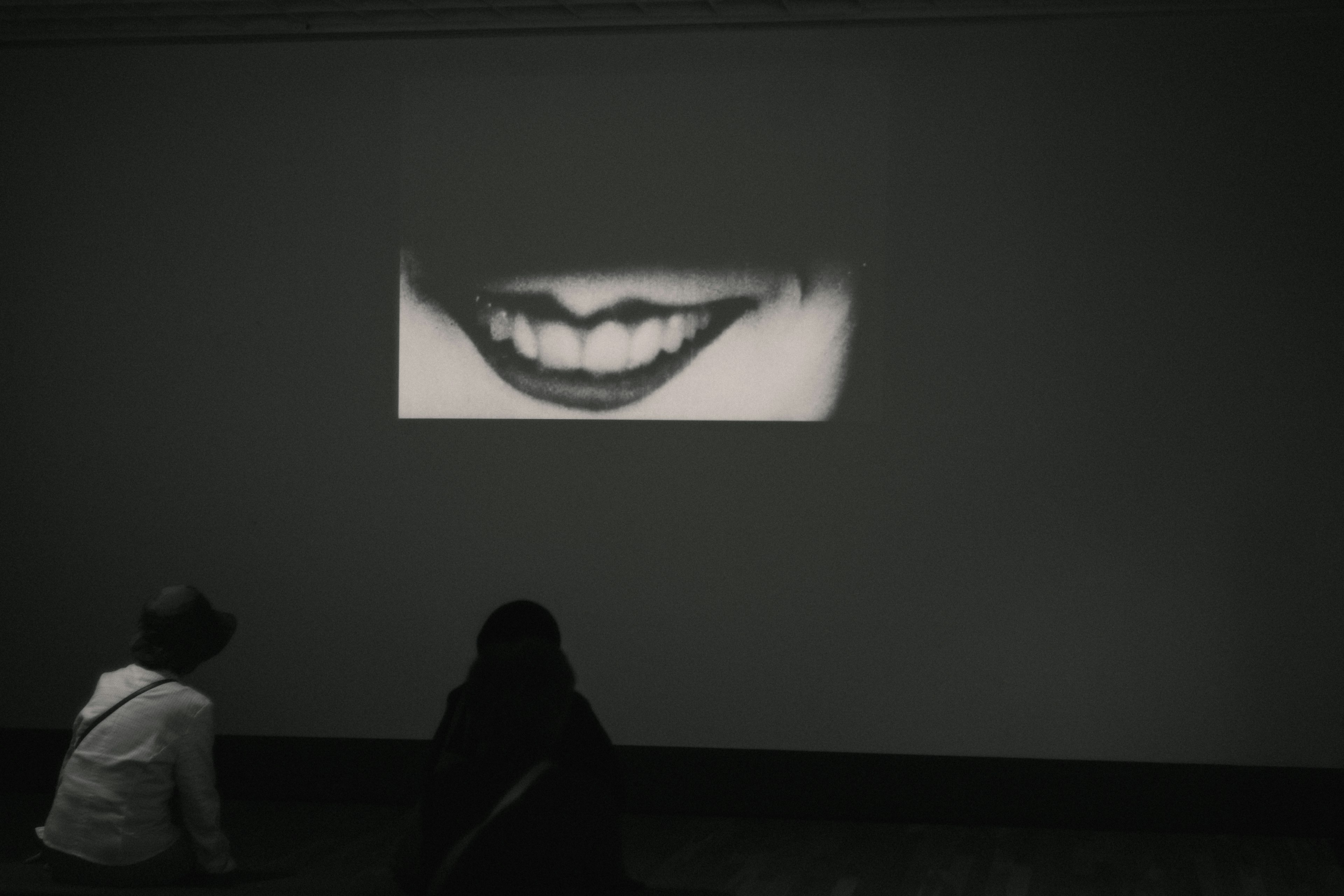 Two viewers gazing at a projected image of a mouth in a dark room