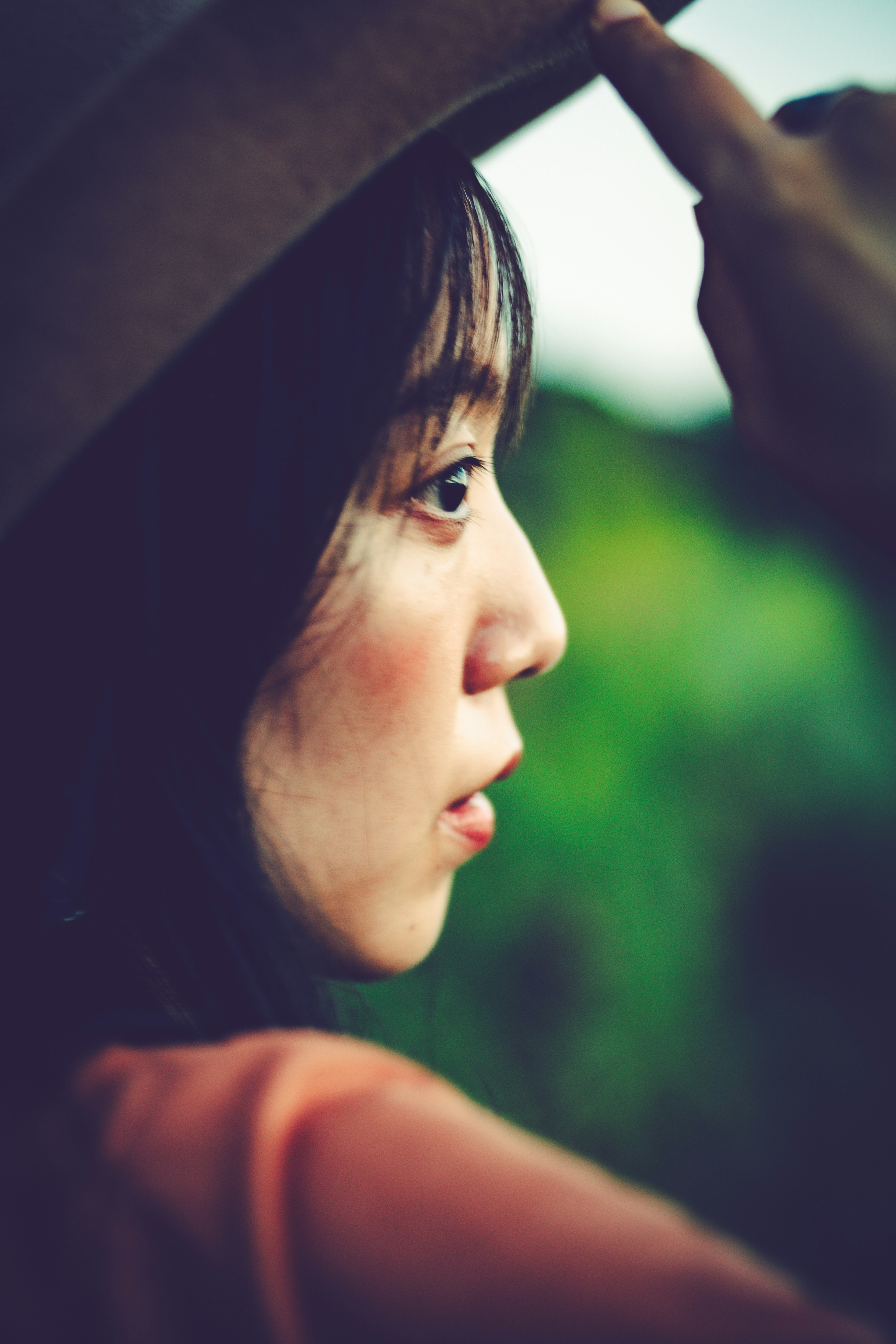 Profile of a woman lifting her hat with a green background and soft lighting