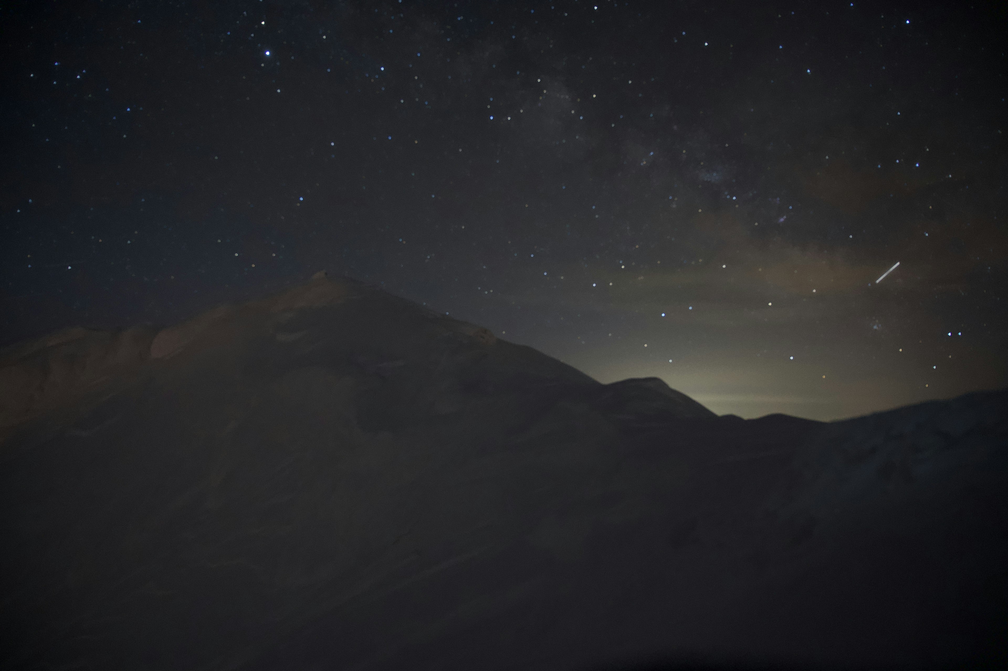 星空の下にある山のシルエットと遠くに輝く光