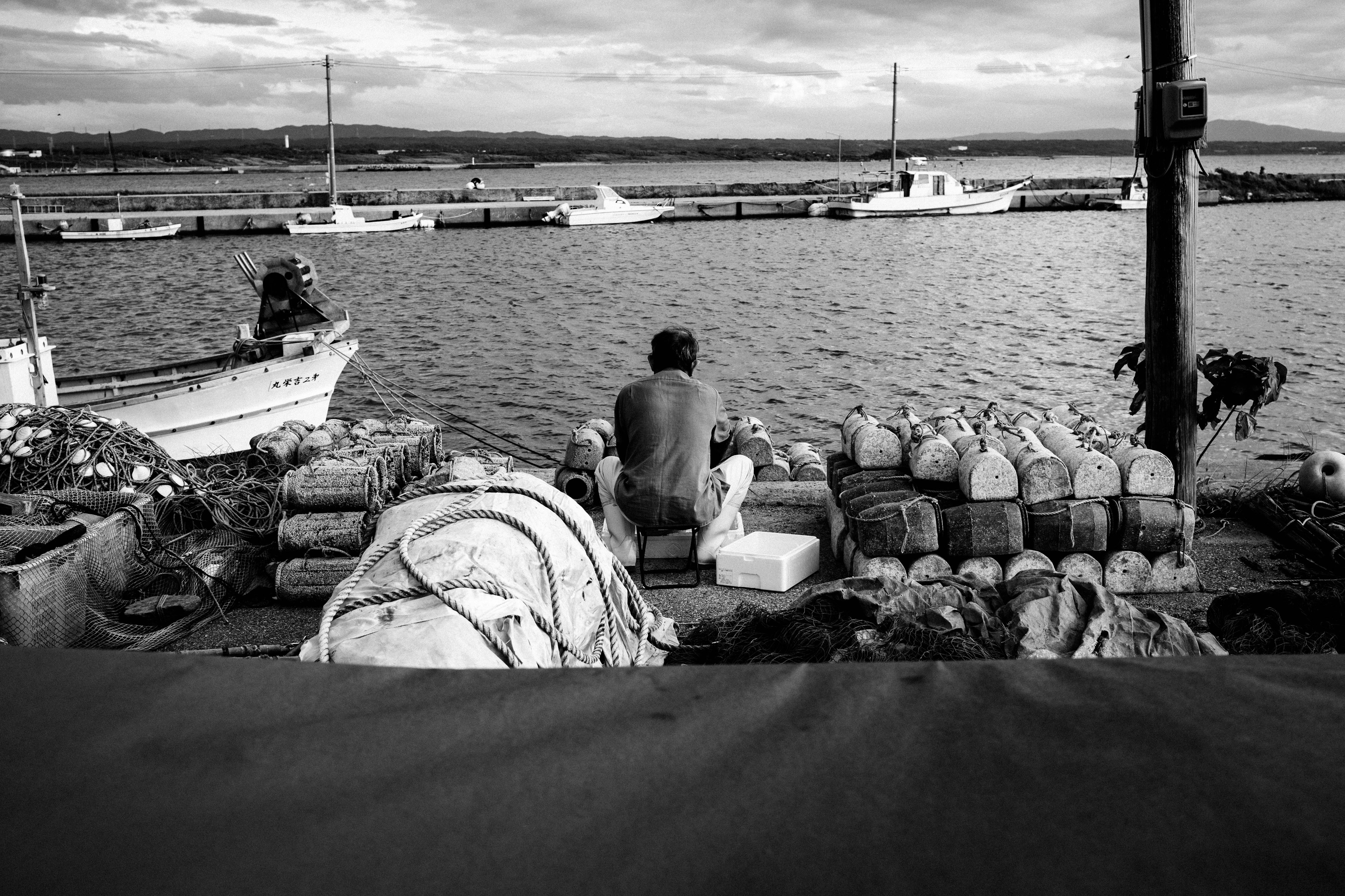 Black and white image of a man working by the seaside with fishing boats