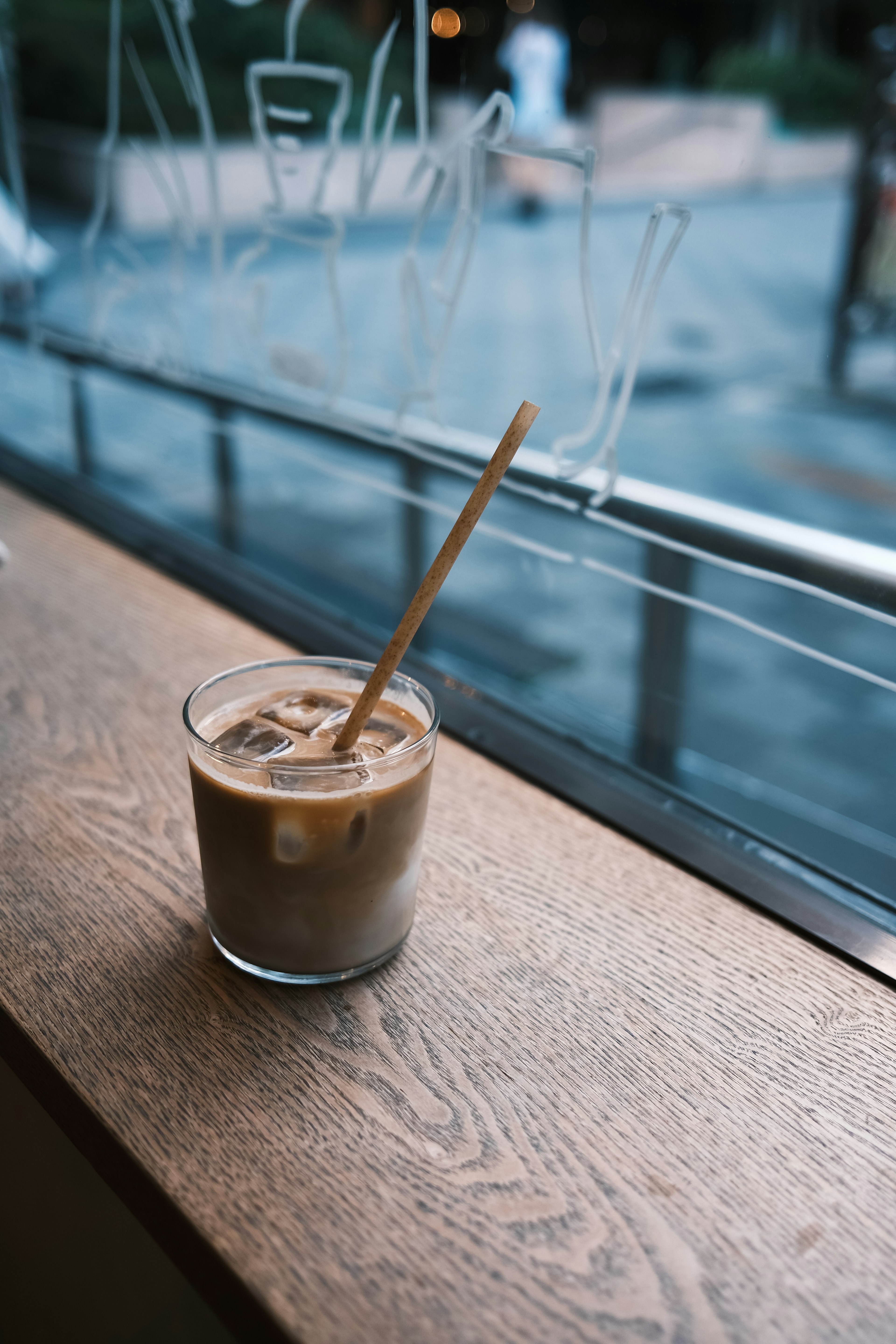 Glas mit Eis-Kaffee und einem Strohhalm auf einem Holzfensterbrett