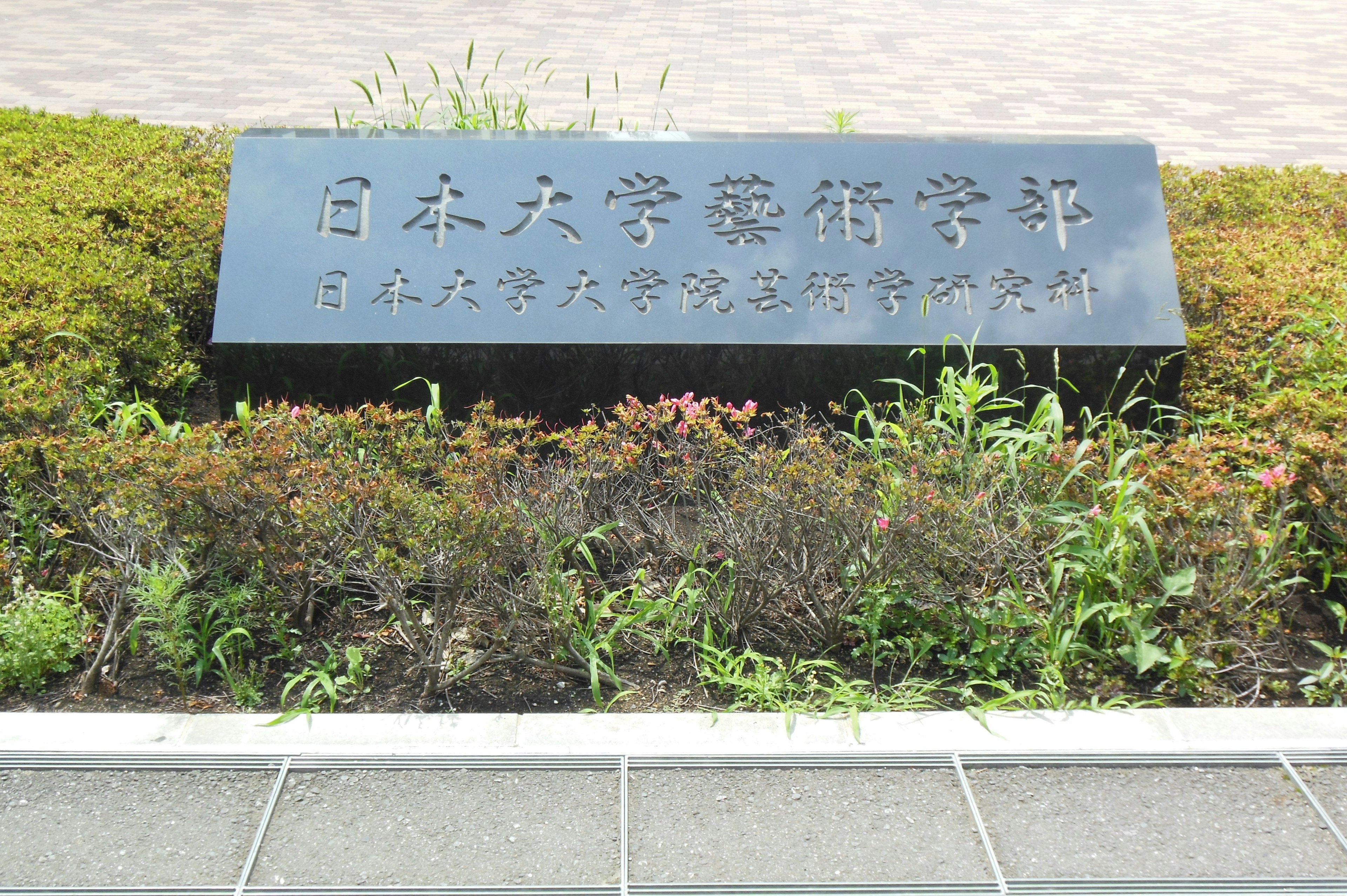 Black sign of Nihon University College of Arts with surrounding green plants