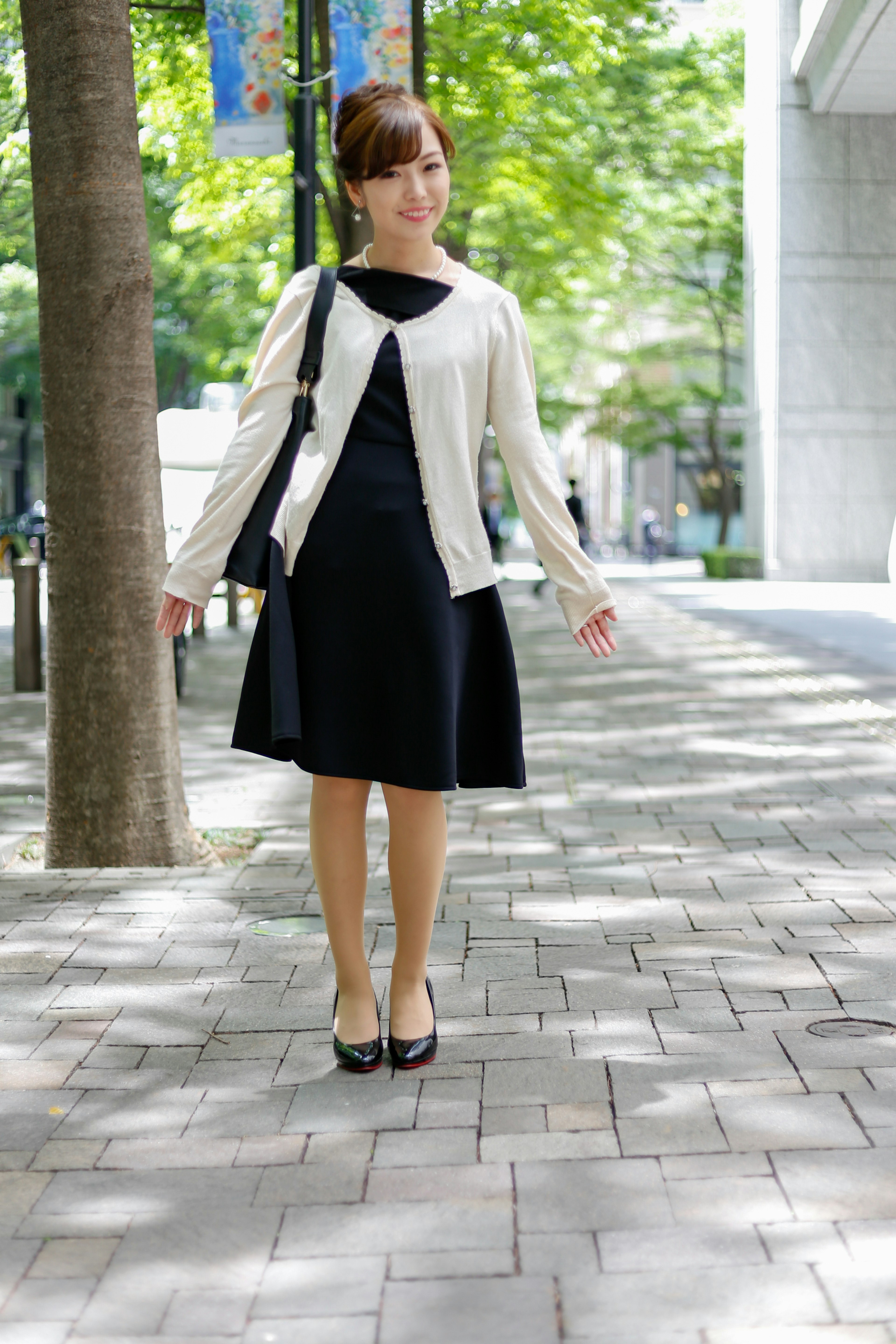 A woman wearing a black dress and white cardigan in an urban setting