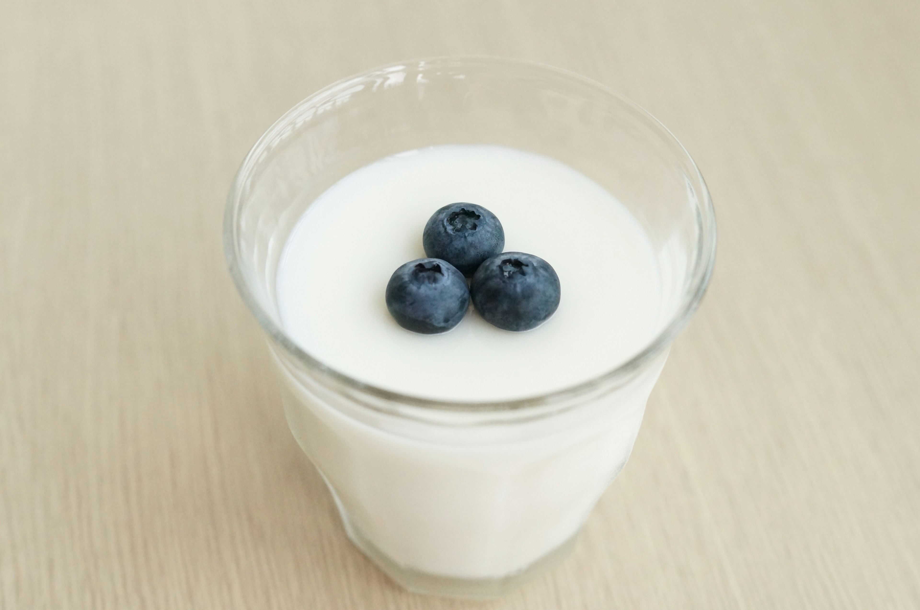 Ein Glas Joghurt, das mit drei Heidelbeeren garniert ist