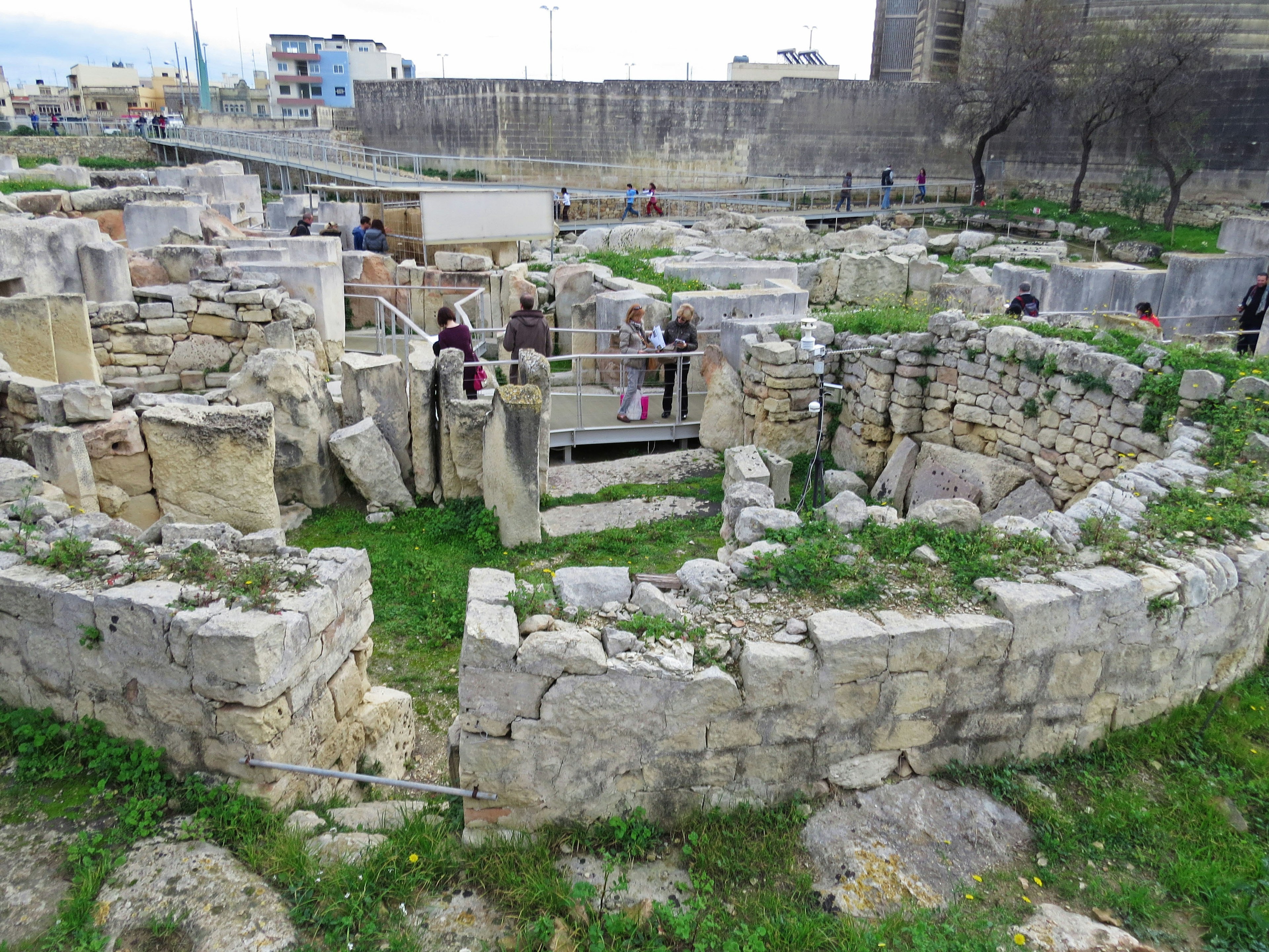 Personas explorando una estructura circular de ruinas rodeada de hierba verde