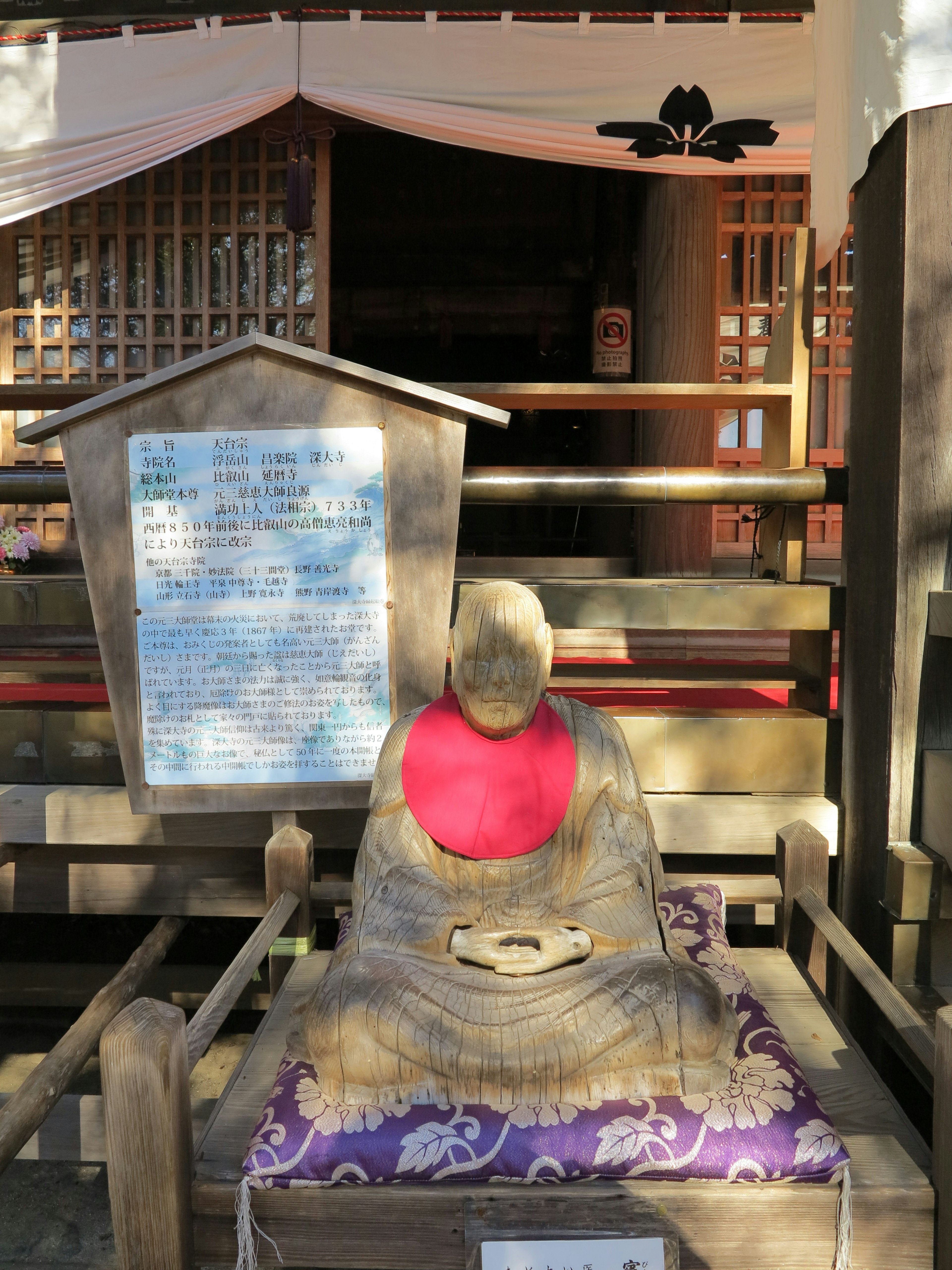 Banc en bois avec une statue de Bouddha assise portant une écharpe rouge