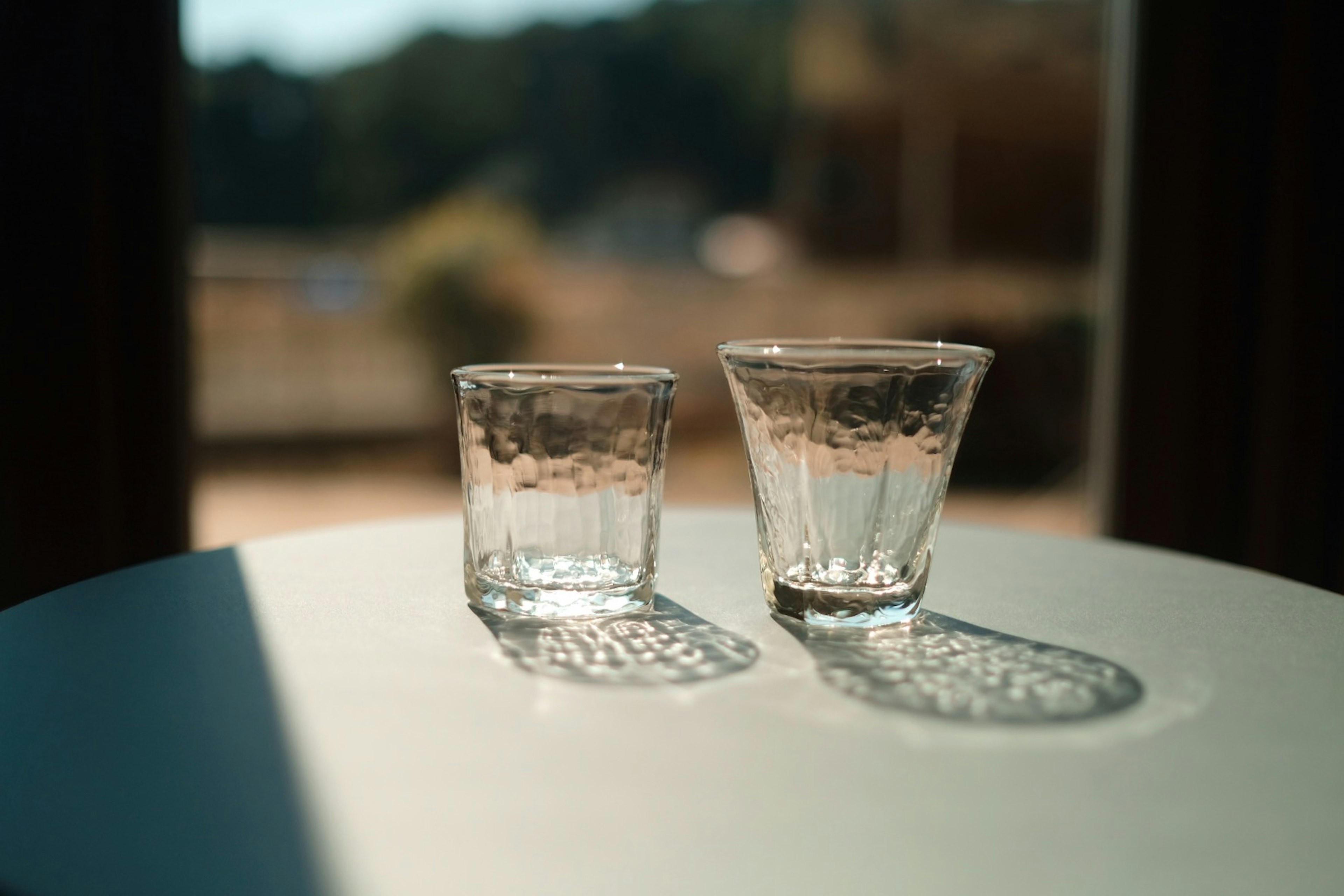 Two clear glasses on a table casting shadows