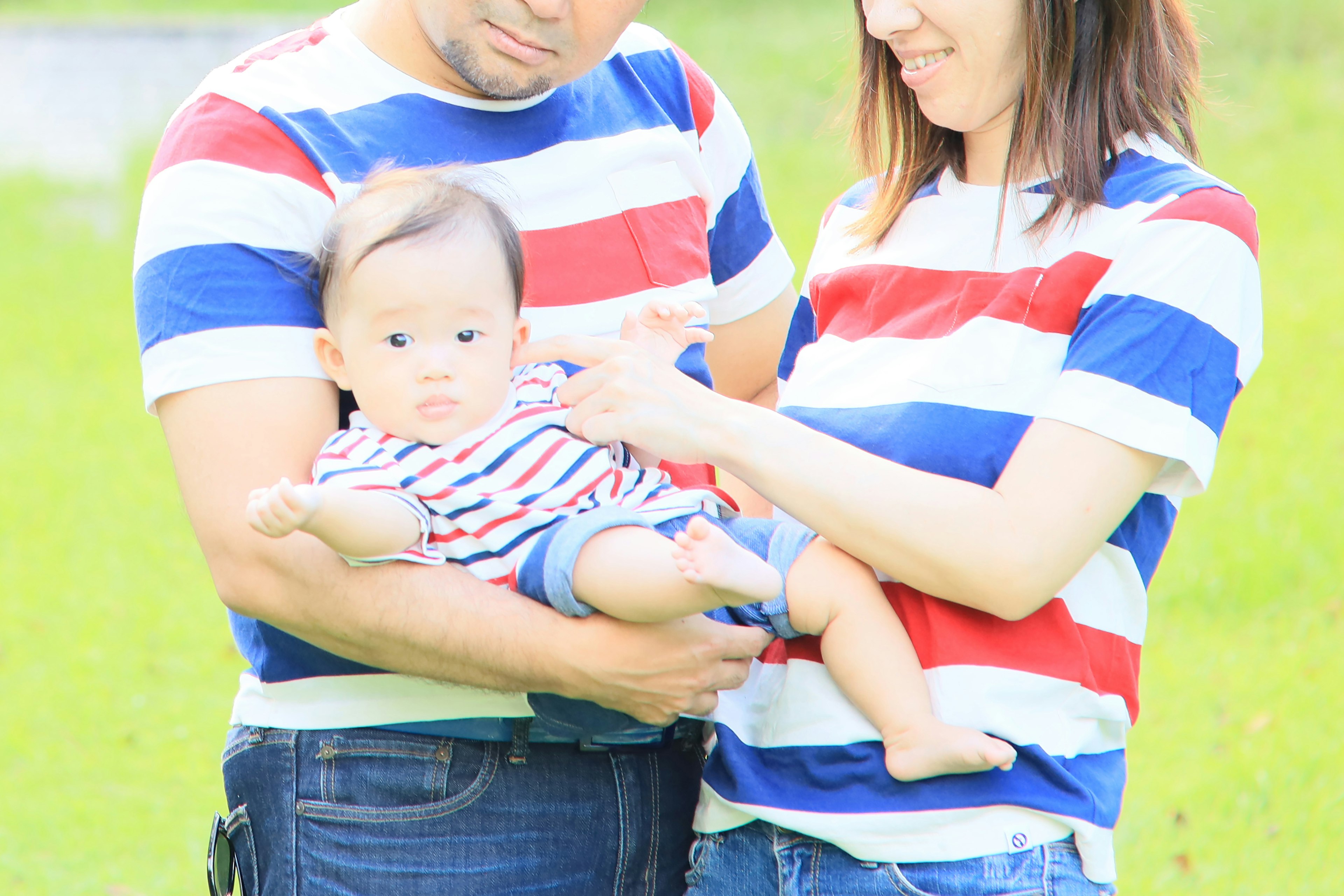 Familia con camisetas a rayas rojas y azules sosteniendo a un bebé en un parque