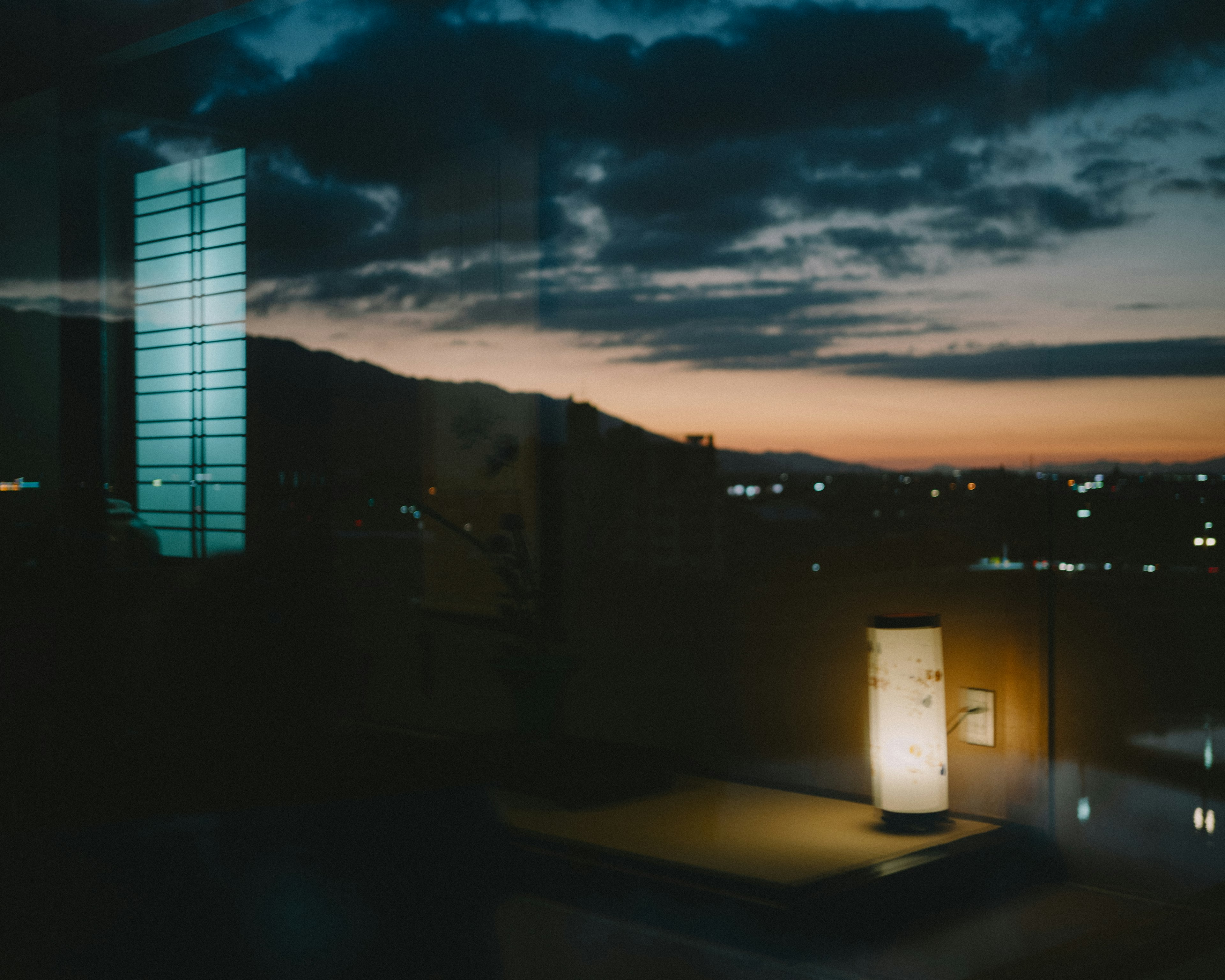 Vista de ventana de un atardecer con una lámpara y luces de la ciudad