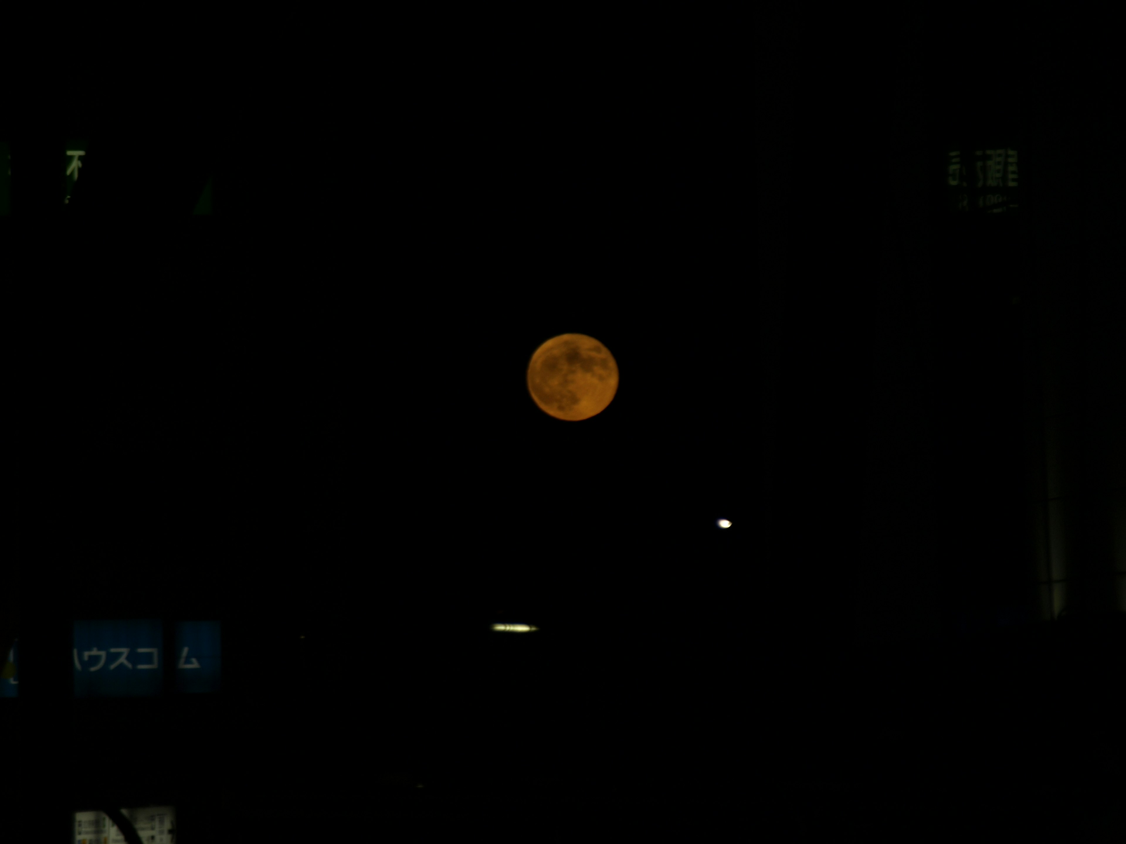 Orange moon visible in a dark sky with building silhouettes