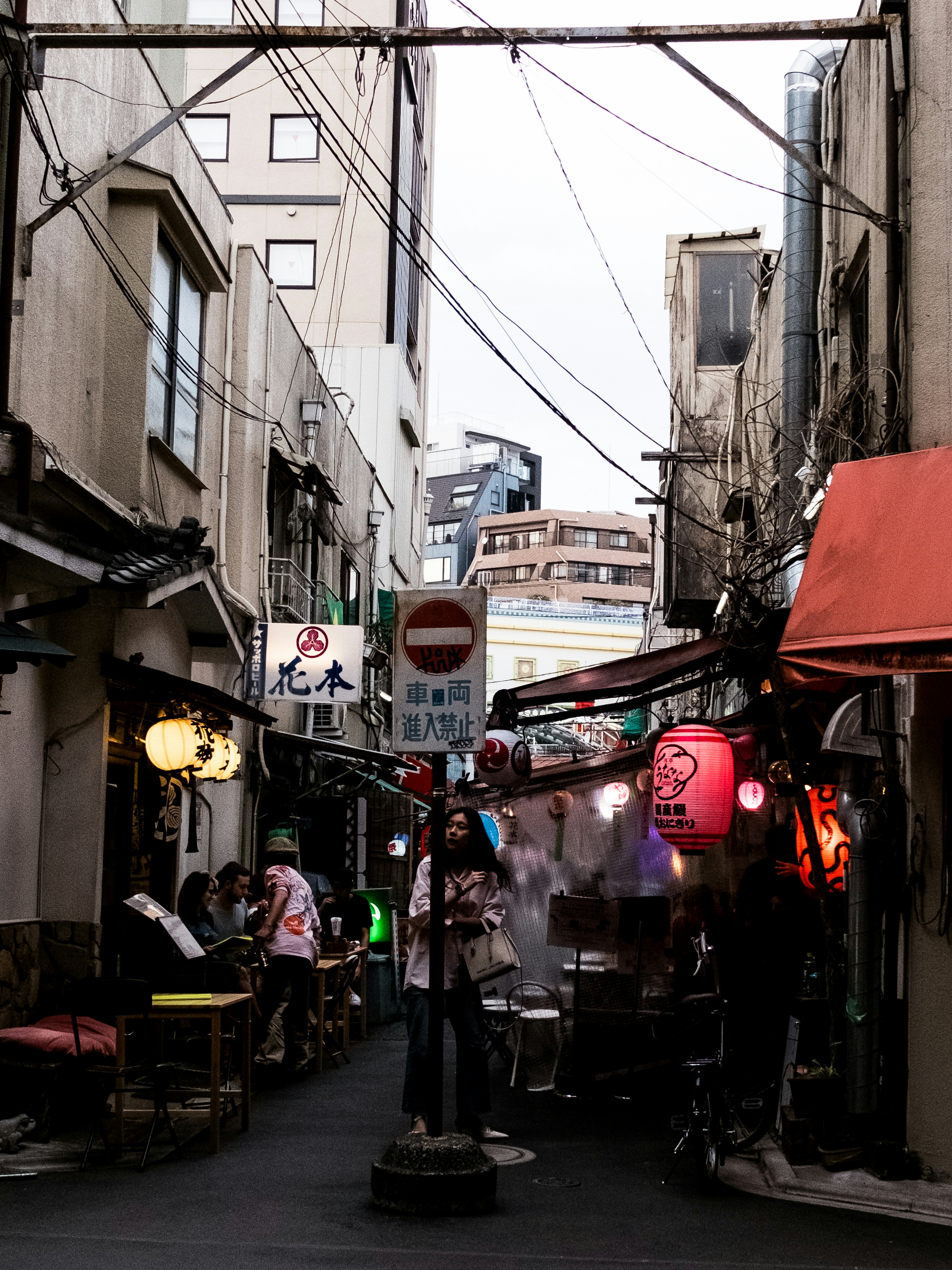 ซอยแคบที่มีแผงขายอาหารและร้านอาหาร โคมไฟและป้ายสว่างสว่างให้กับบรรยากาศยามค่ำคืนของญี่ปุ่น