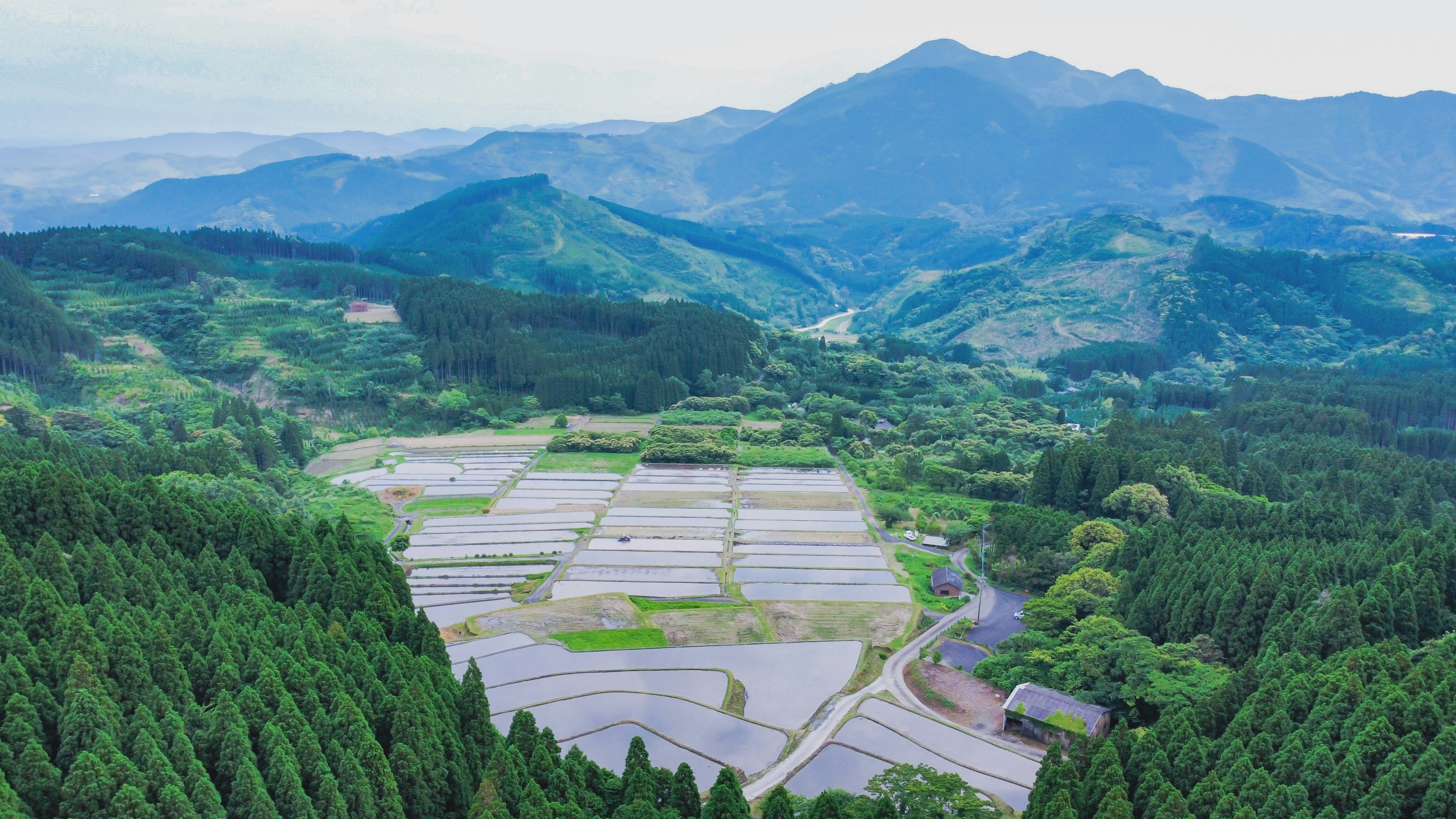 Aerial view of a picturesque rural landscape surrounded by mountains featuring lush forests and rice paddies