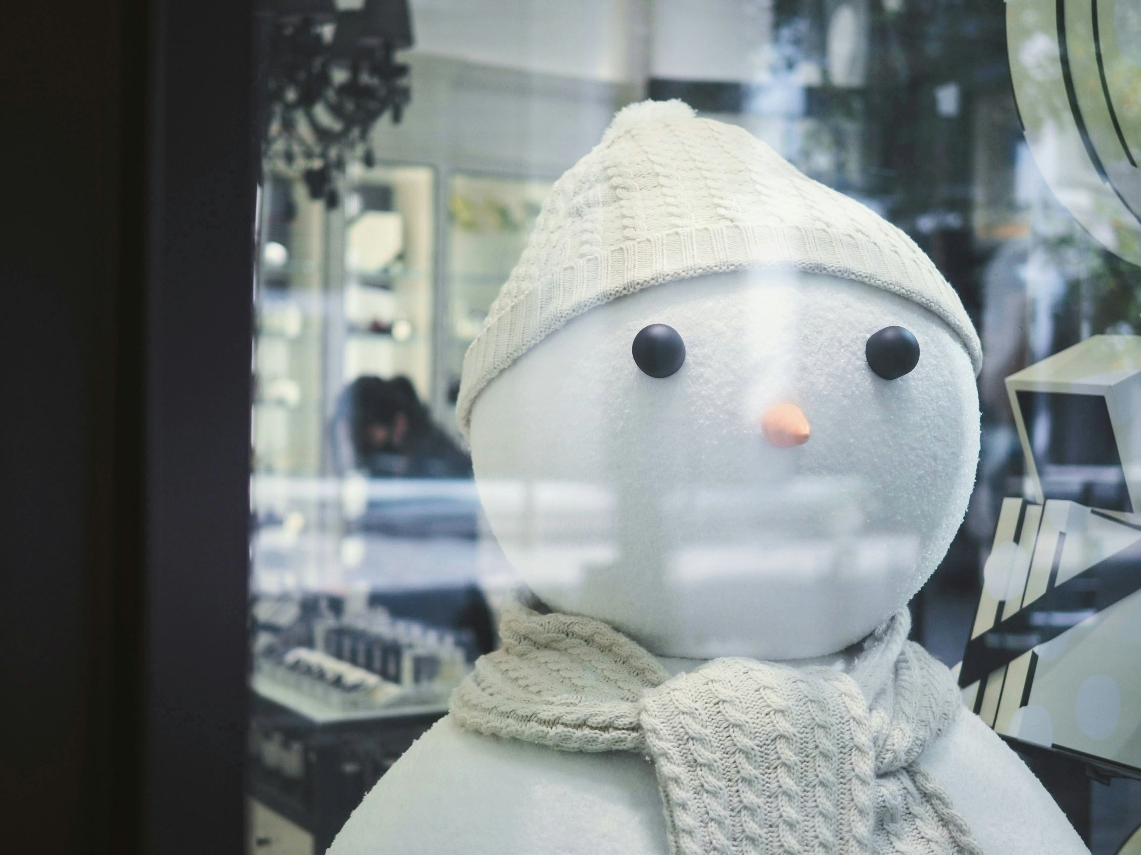 A white snowman wearing a knitted hat and scarf displayed in a shop window