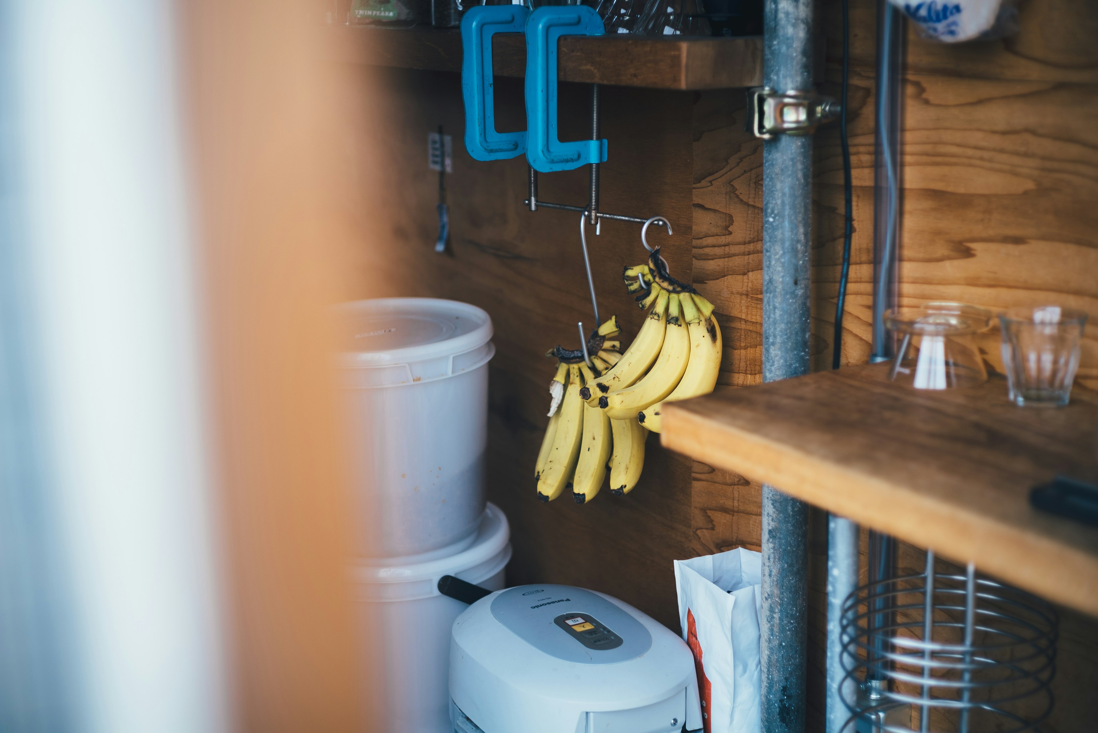 A wooden shelf with hanging bananas and kitchen items in a small space