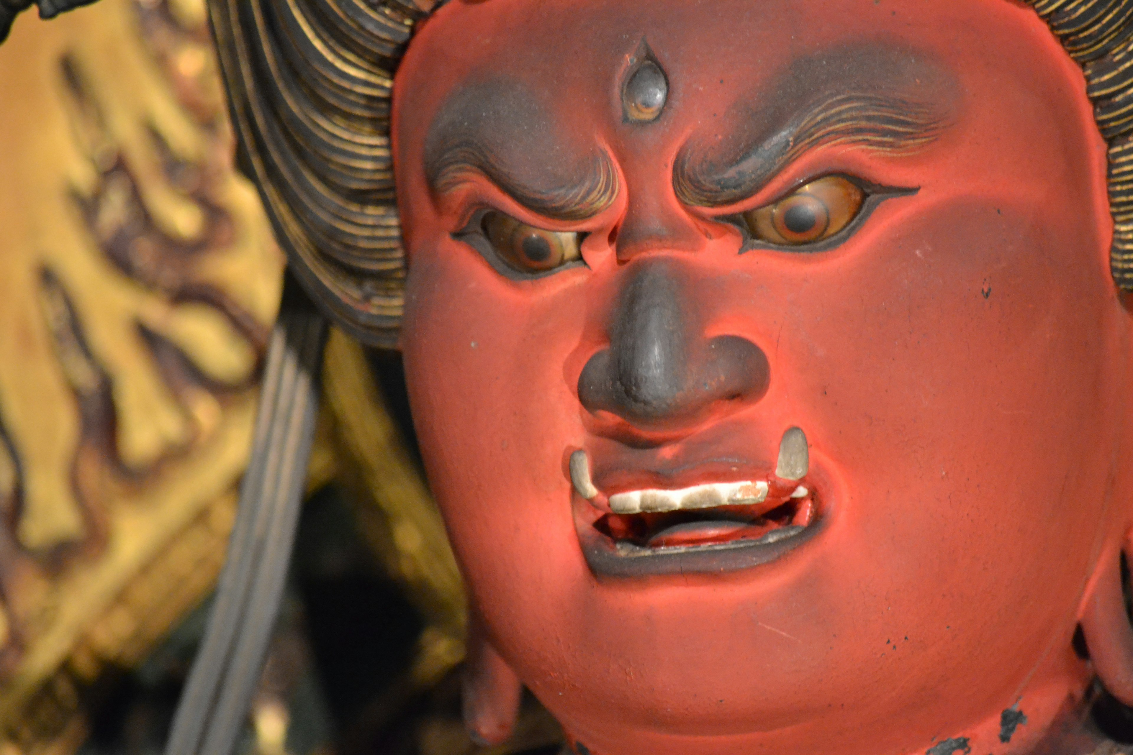 Primer plano de una estatua de deidad con rostro rojo y expresión enojada con dientes afilados