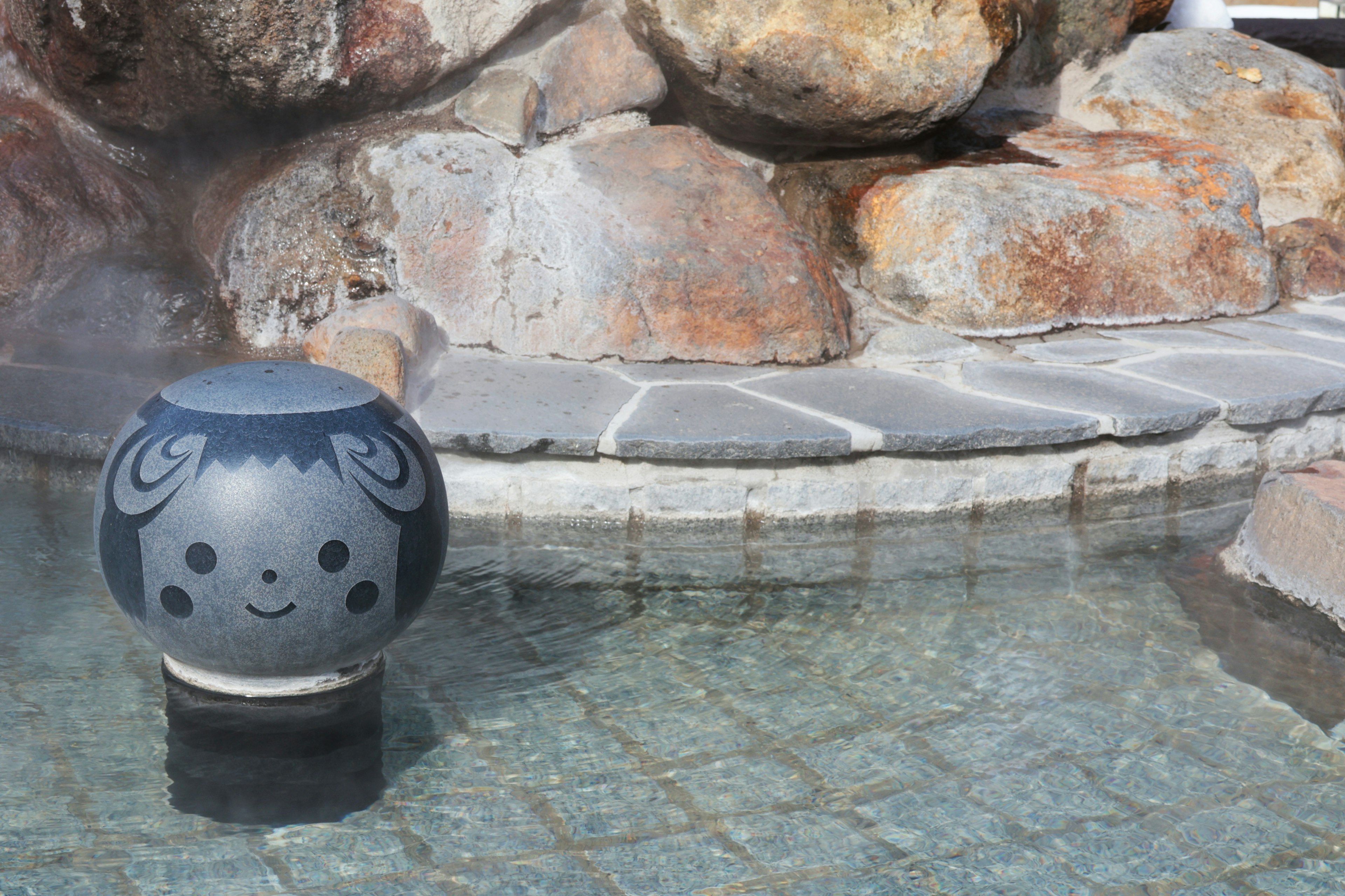 Bola de piedra con un personaje lindo flotando en el agua de una fuente termal rodeada de rocas