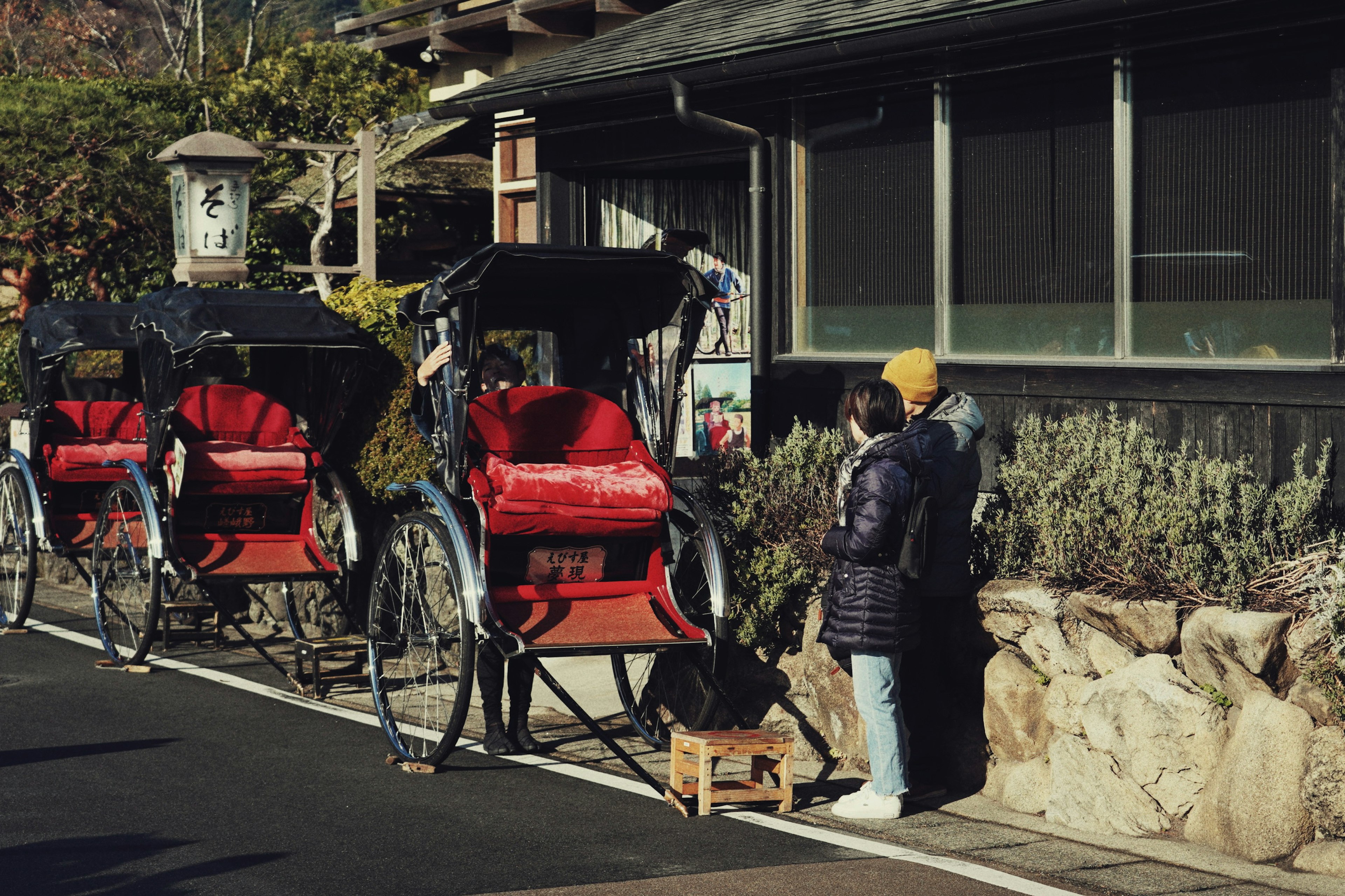 Dos personas de pie junto a rickshaws rojos en una calle pintoresca