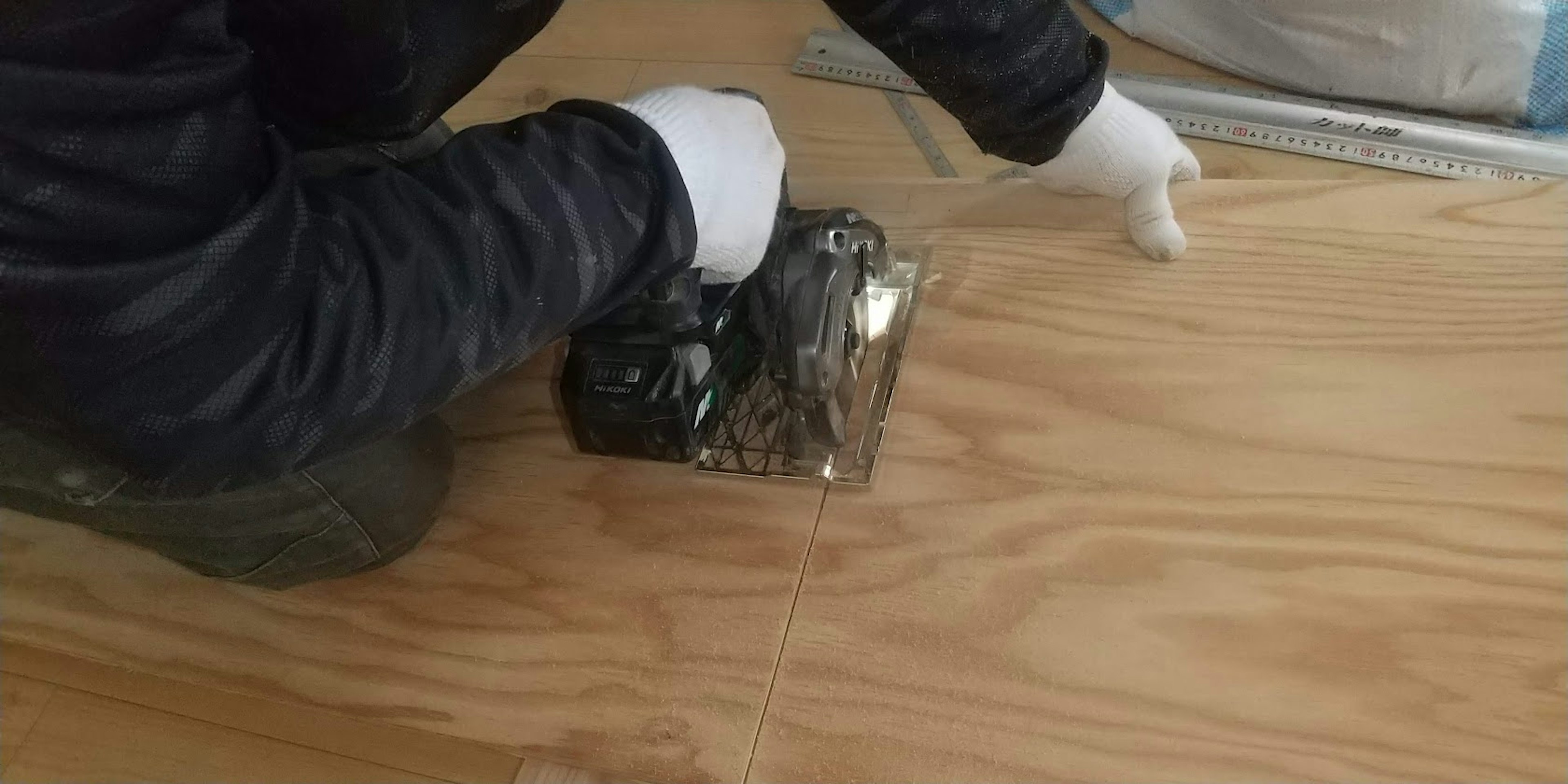 Worker installing wood flooring using tools while wearing gloves