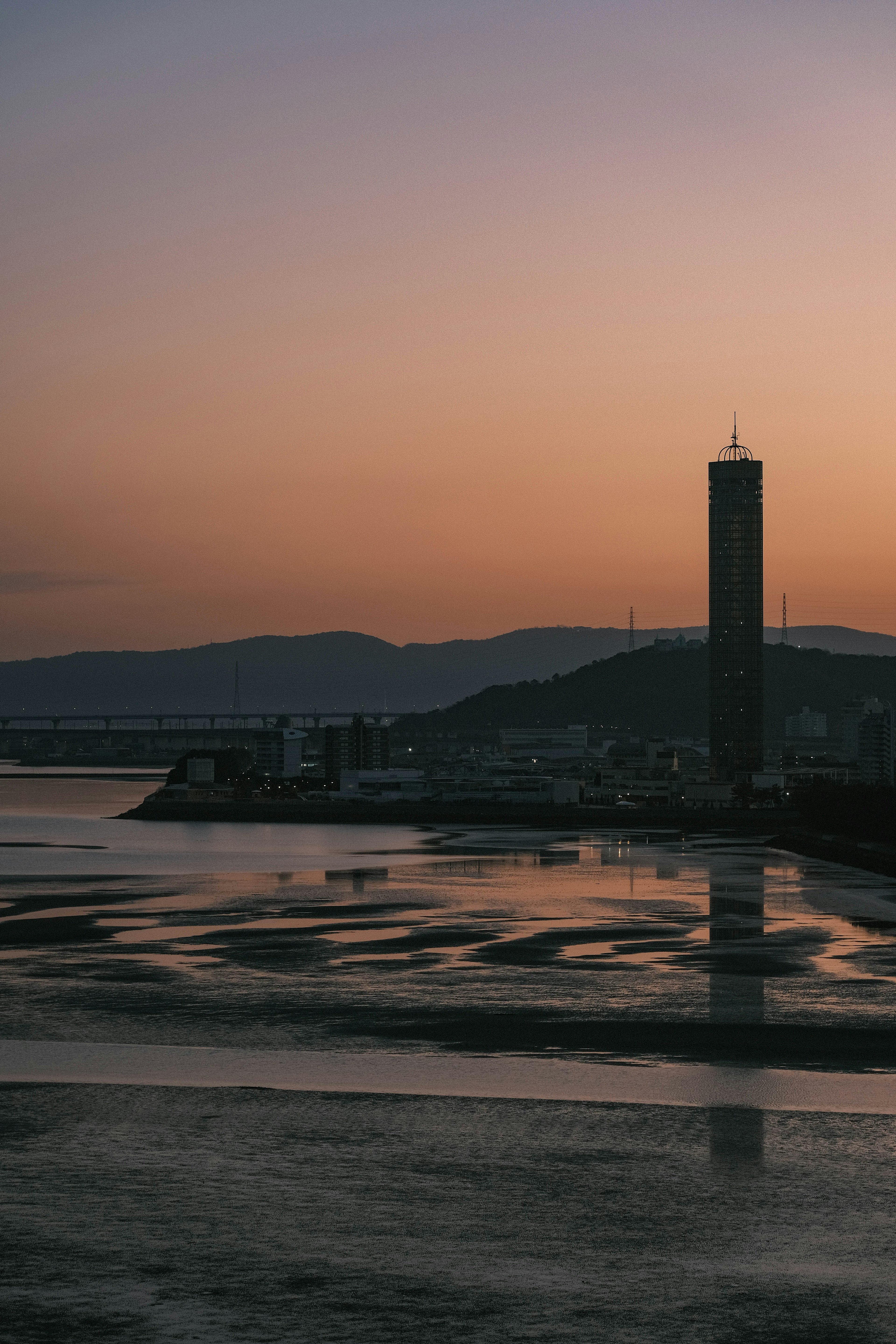 Silhouette eines hohen Turms vor einem Sonnenuntergangsreflex auf dem Fluss