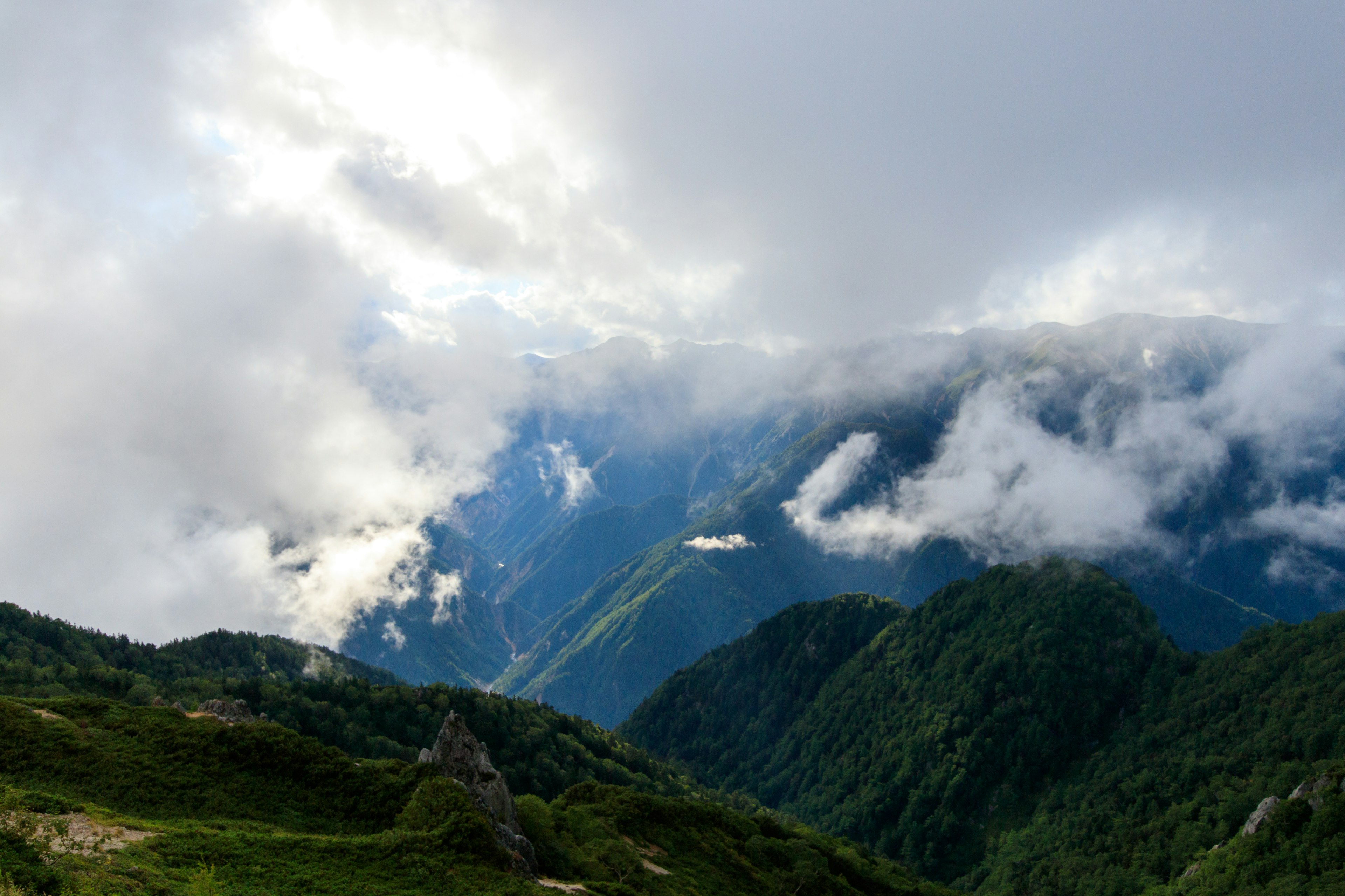 Una vista impresionante de montañas cubiertas de nubes con colinas y valles verdes