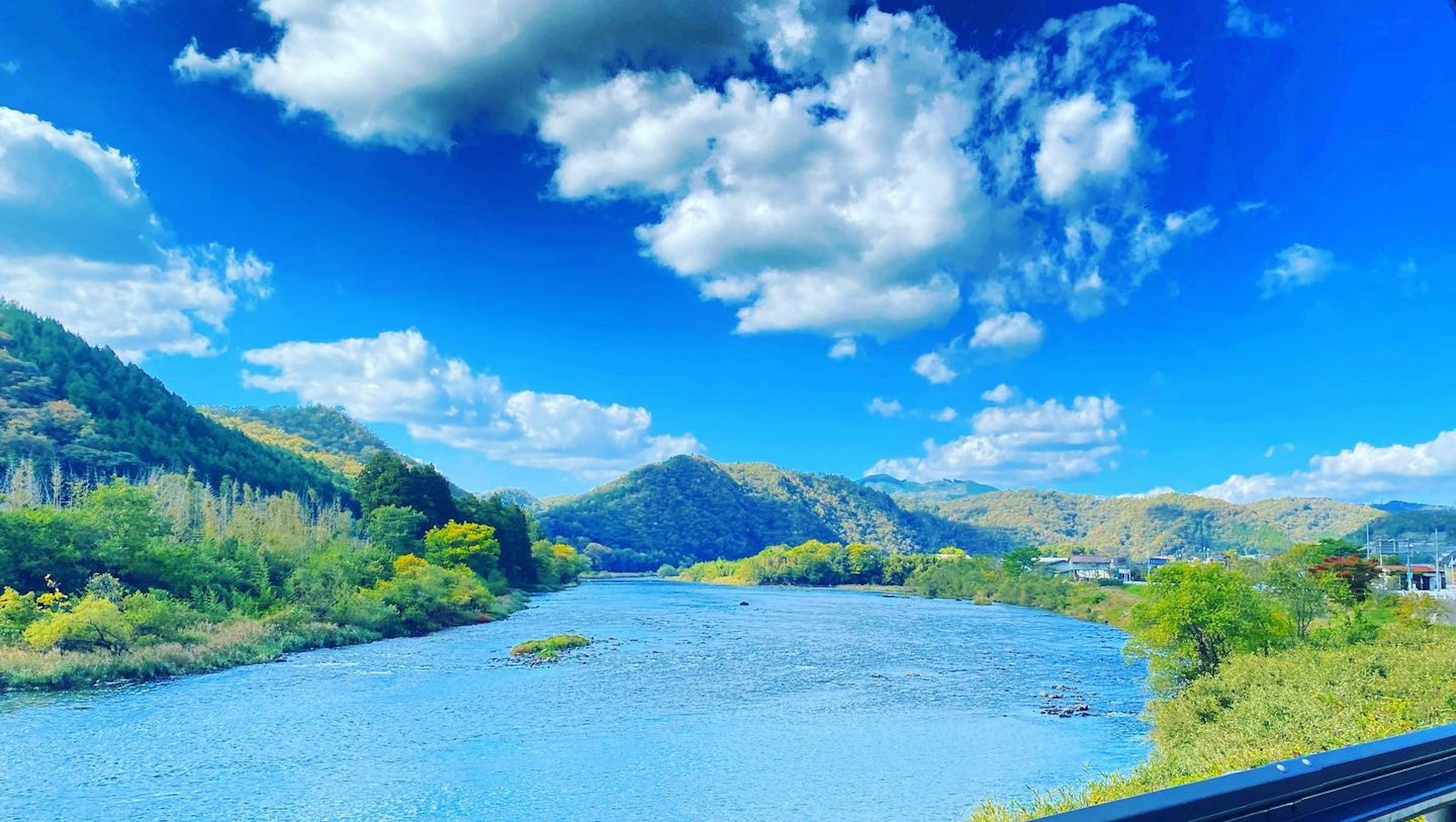 Pemandangan sungai yang indah dengan langit biru dan awan dikelilingi perbukitan hijau