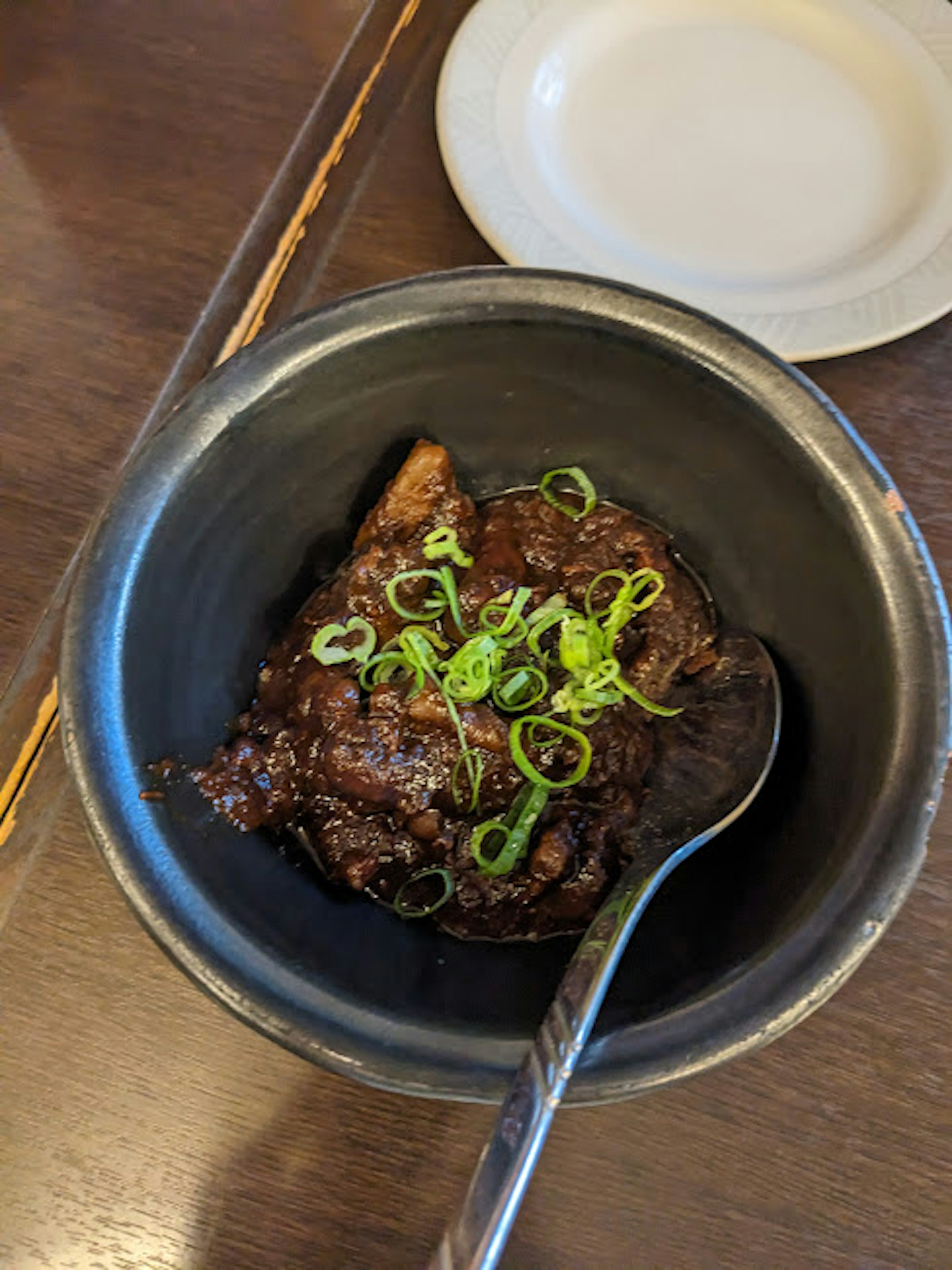 黒い鍋に盛られた料理に青ねぎがトッピングされている