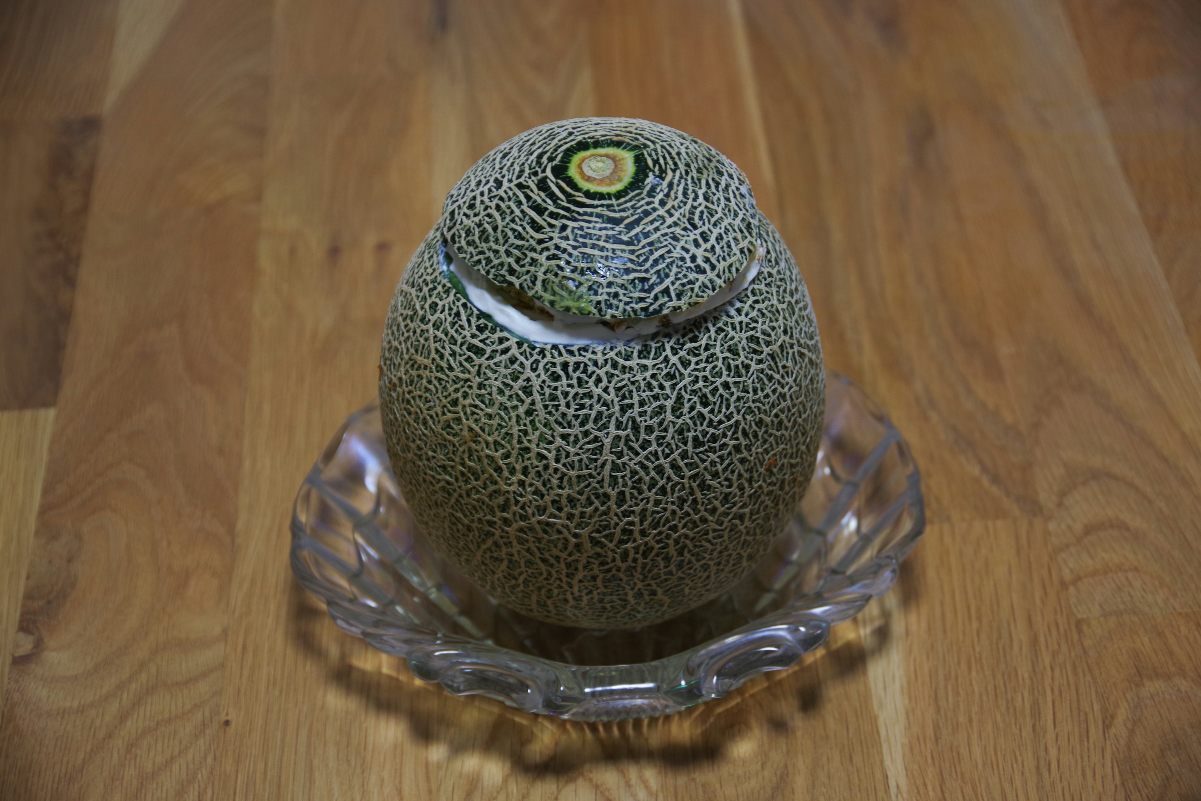 A melon placed on a clear plate on a wooden surface