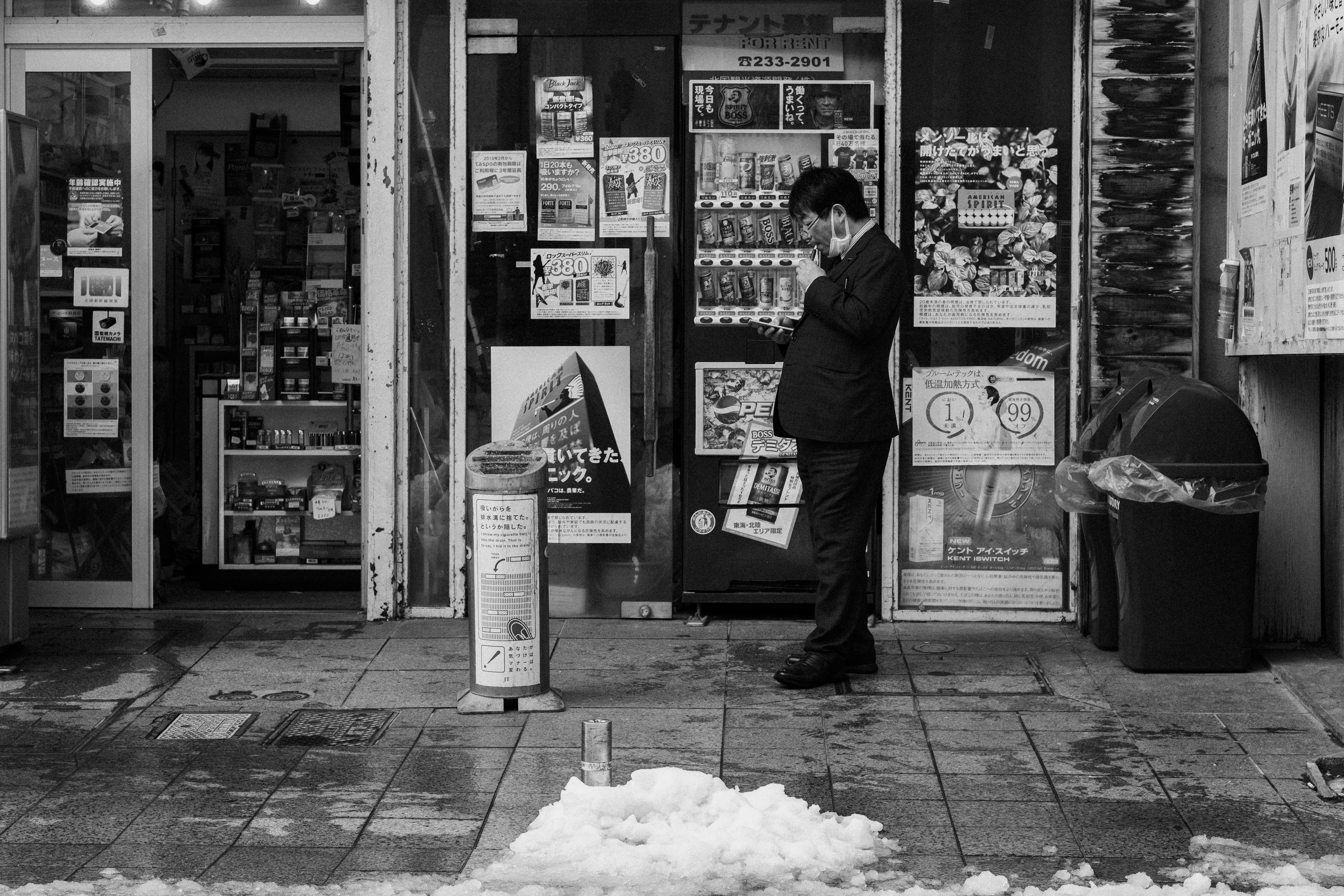 Un uomo in giacca che parla al telefono davanti a un negozio con neve a terra