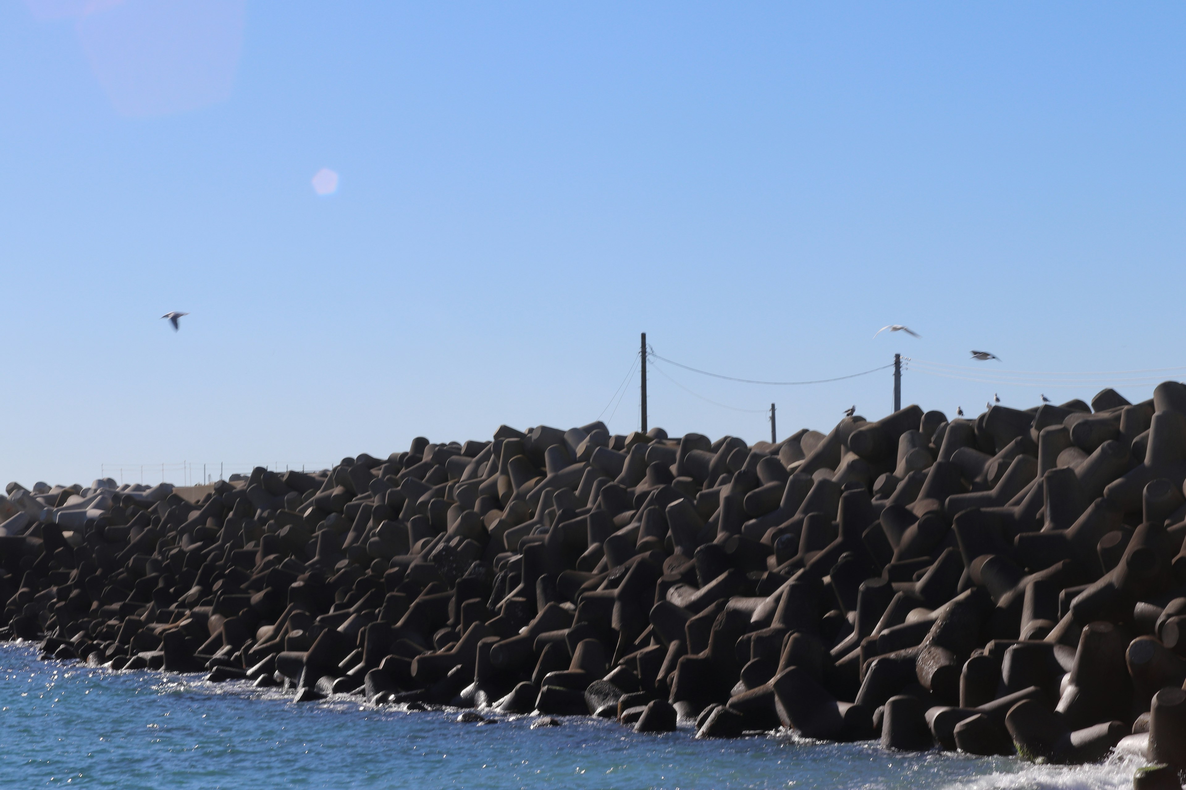 Estructuras de concreto a lo largo de un rompeolas costero bajo un cielo azul claro