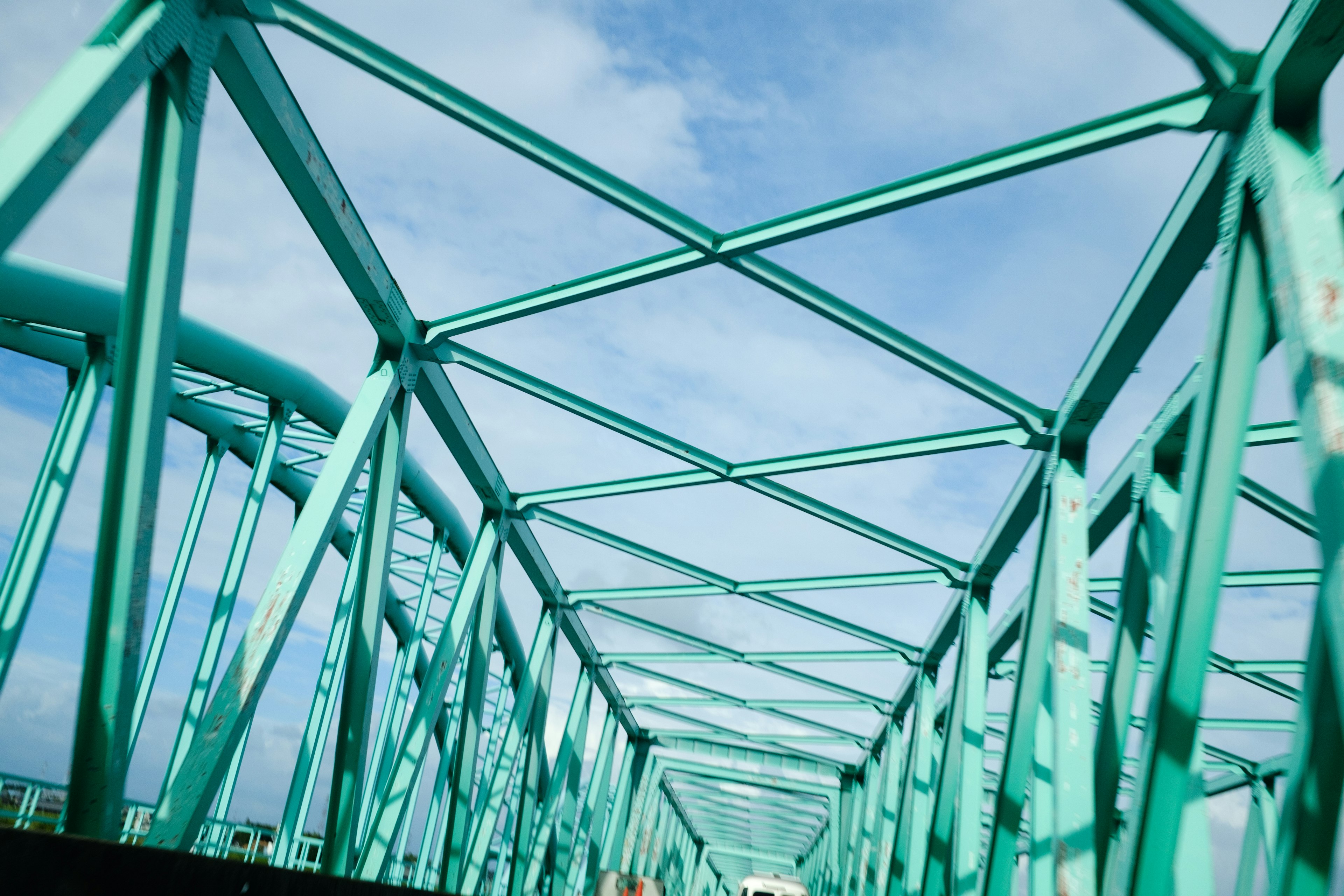 Blick von unten auf eine türkisfarbene Metallbrücke mit blauem Himmel und Wolken