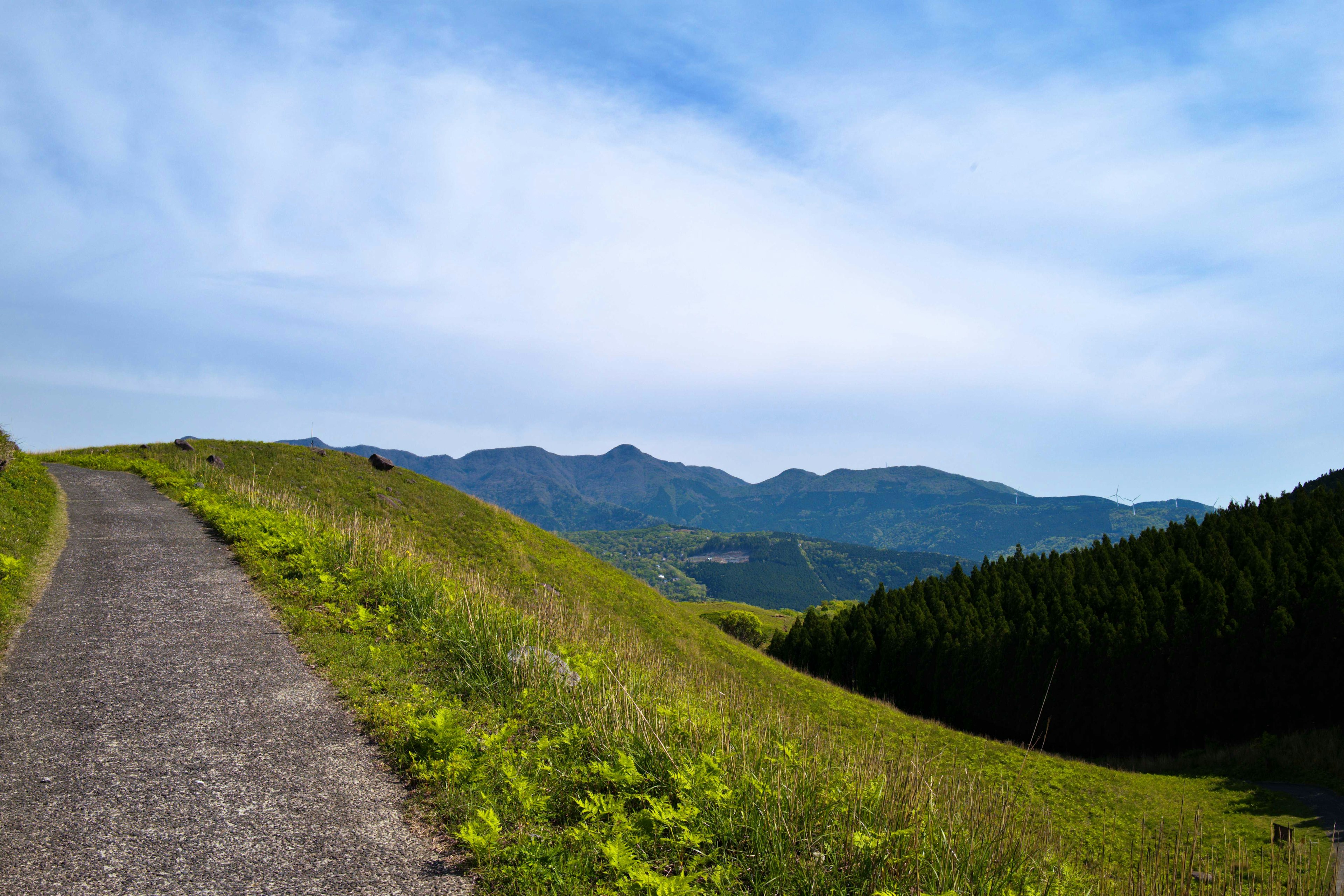 Paved path through green hills under a blue sky