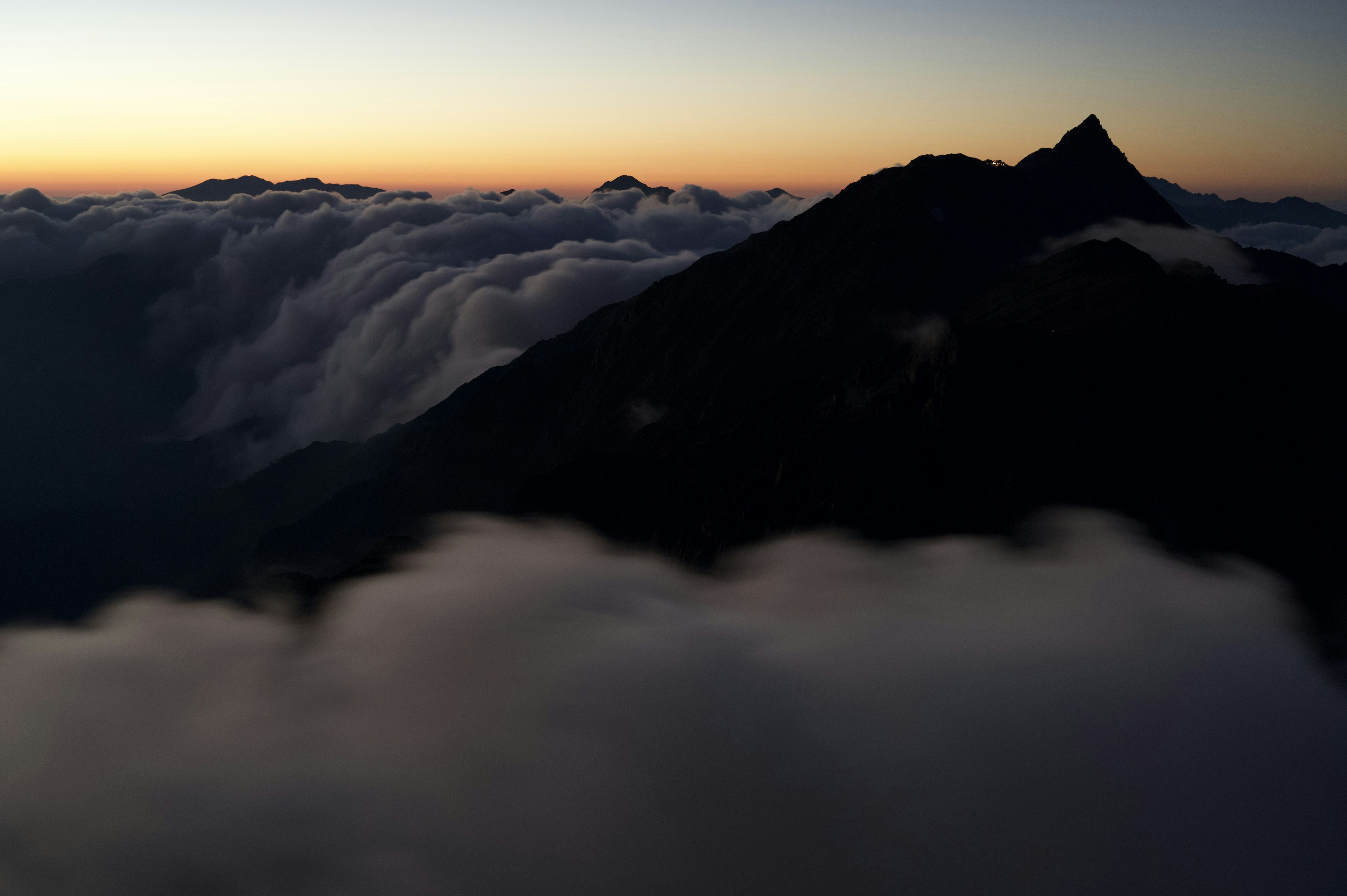 Silhouette di una montagna che si erge sopra le nuvole al tramonto