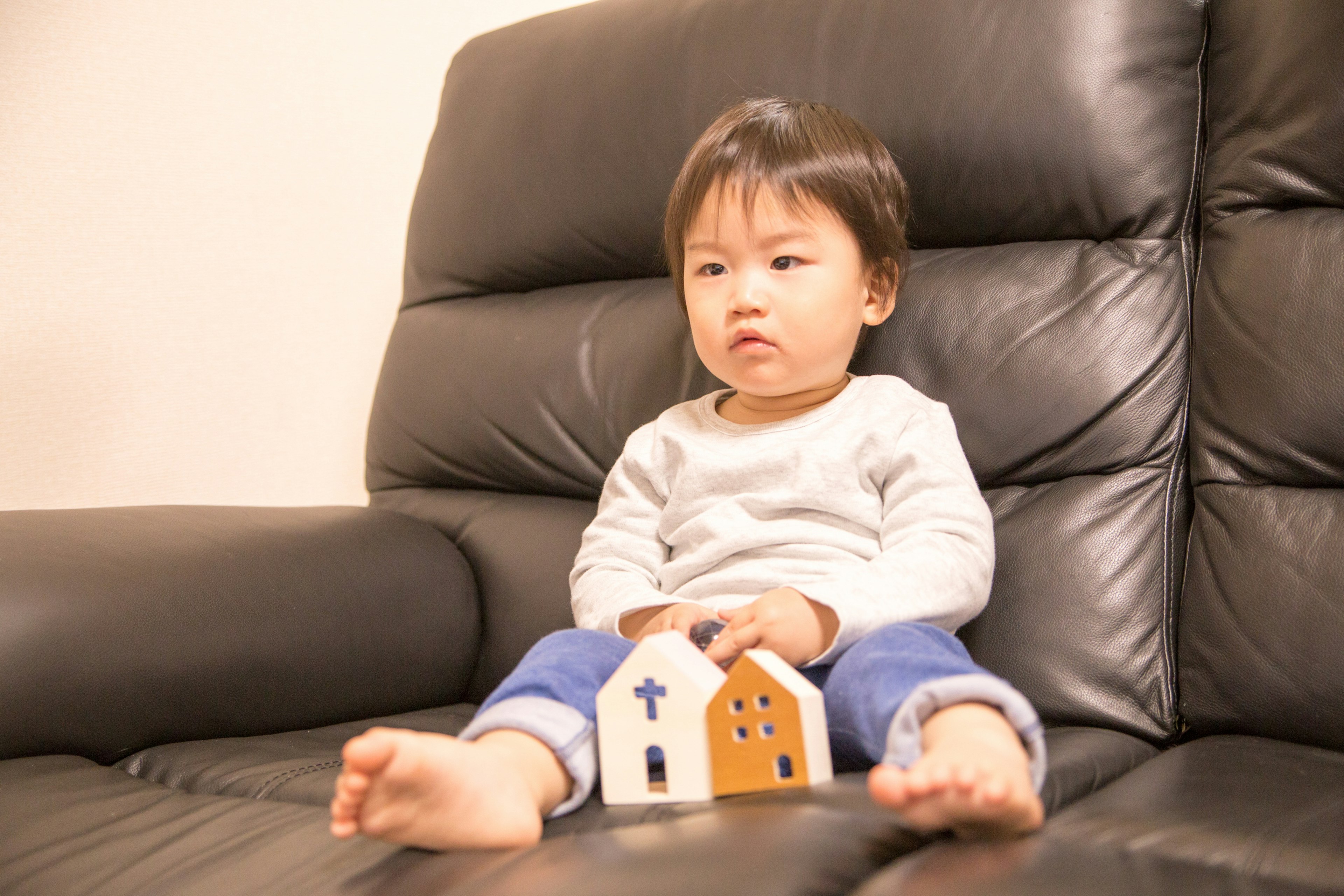 검은 소파에 앉아 나무 집 장난감을 들고 있는 아이