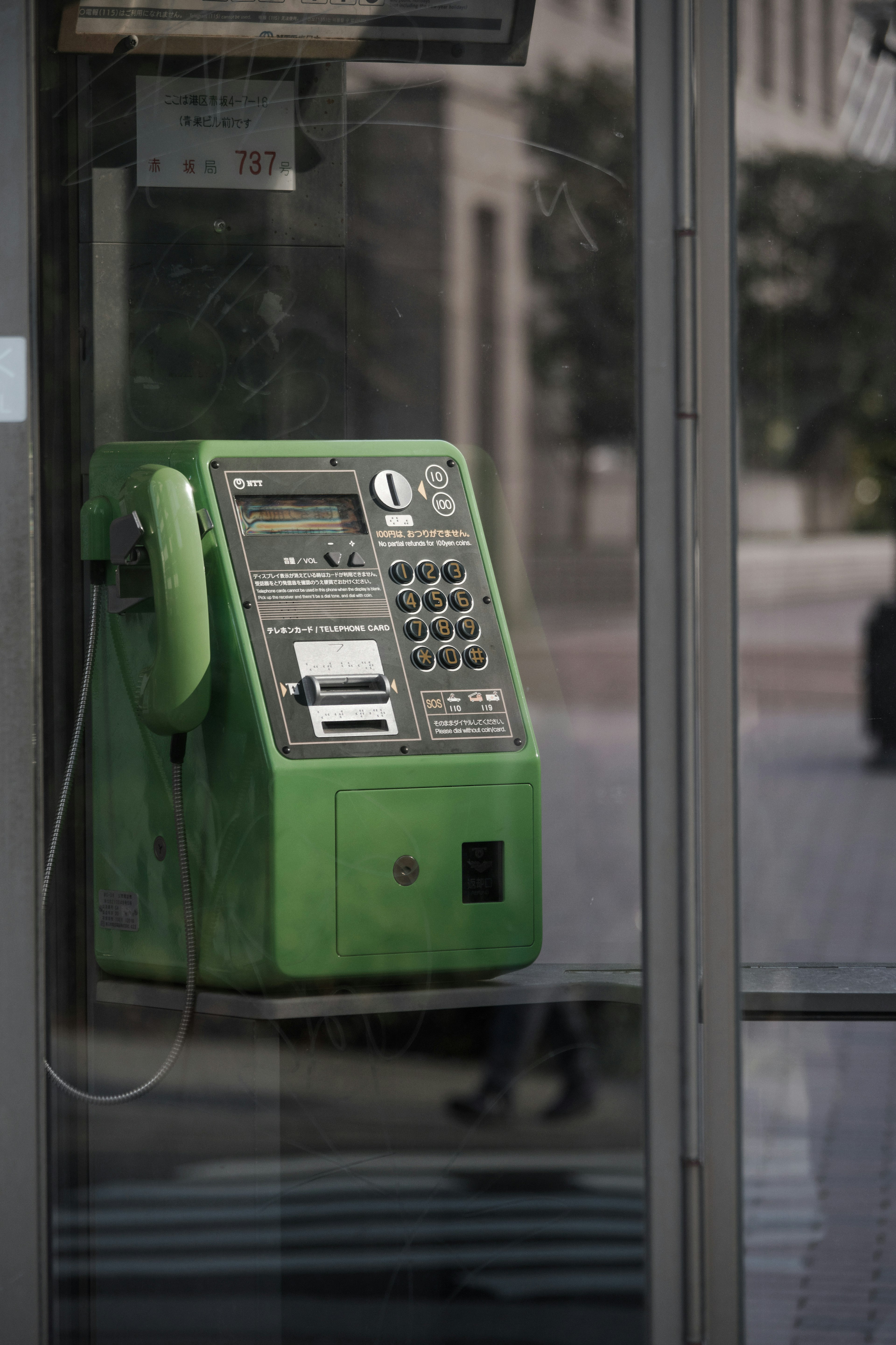 Green public telephone installed in a glass phone booth