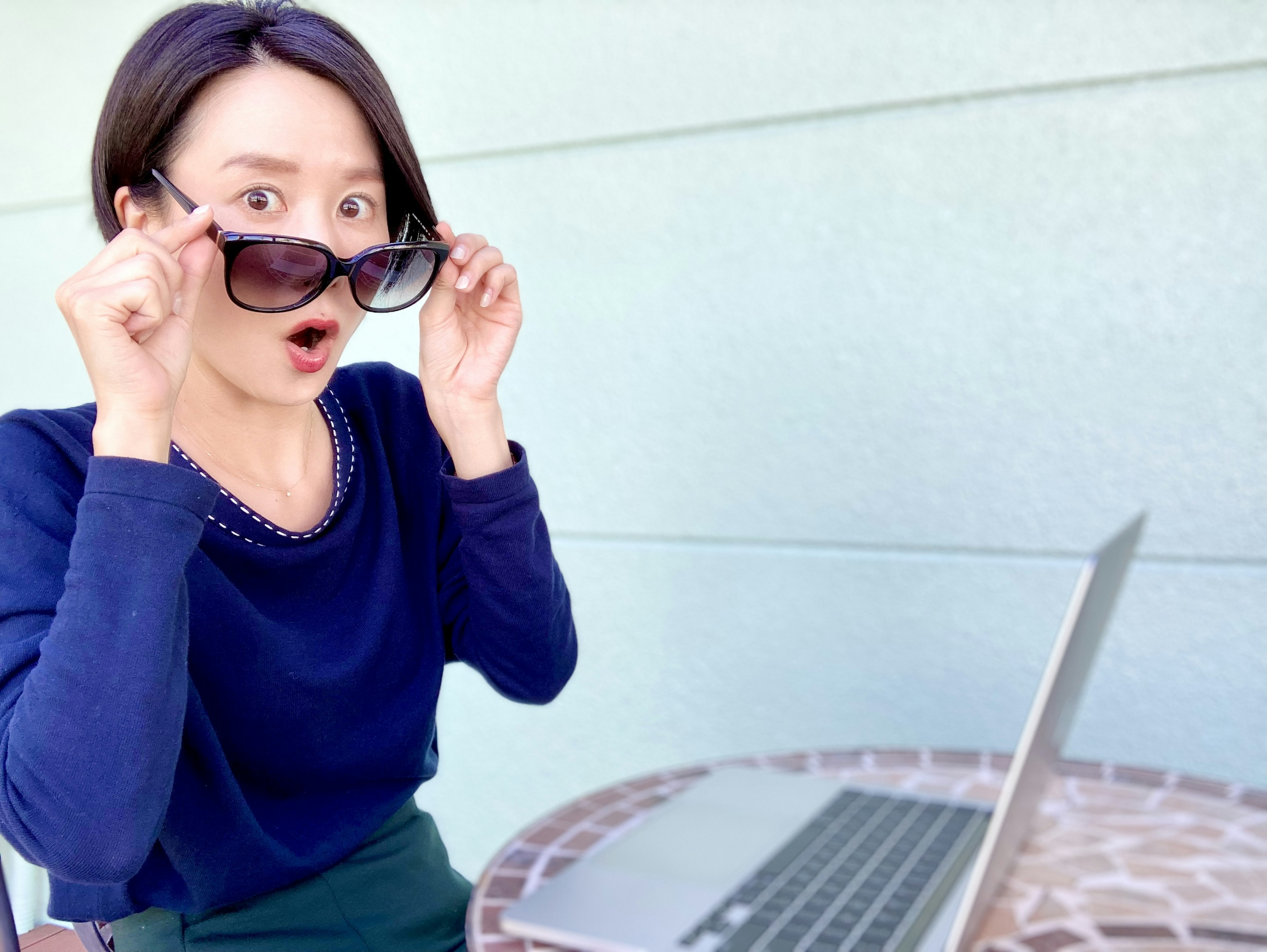 Surprised woman adjusting sunglasses while sitting at a table with a laptop