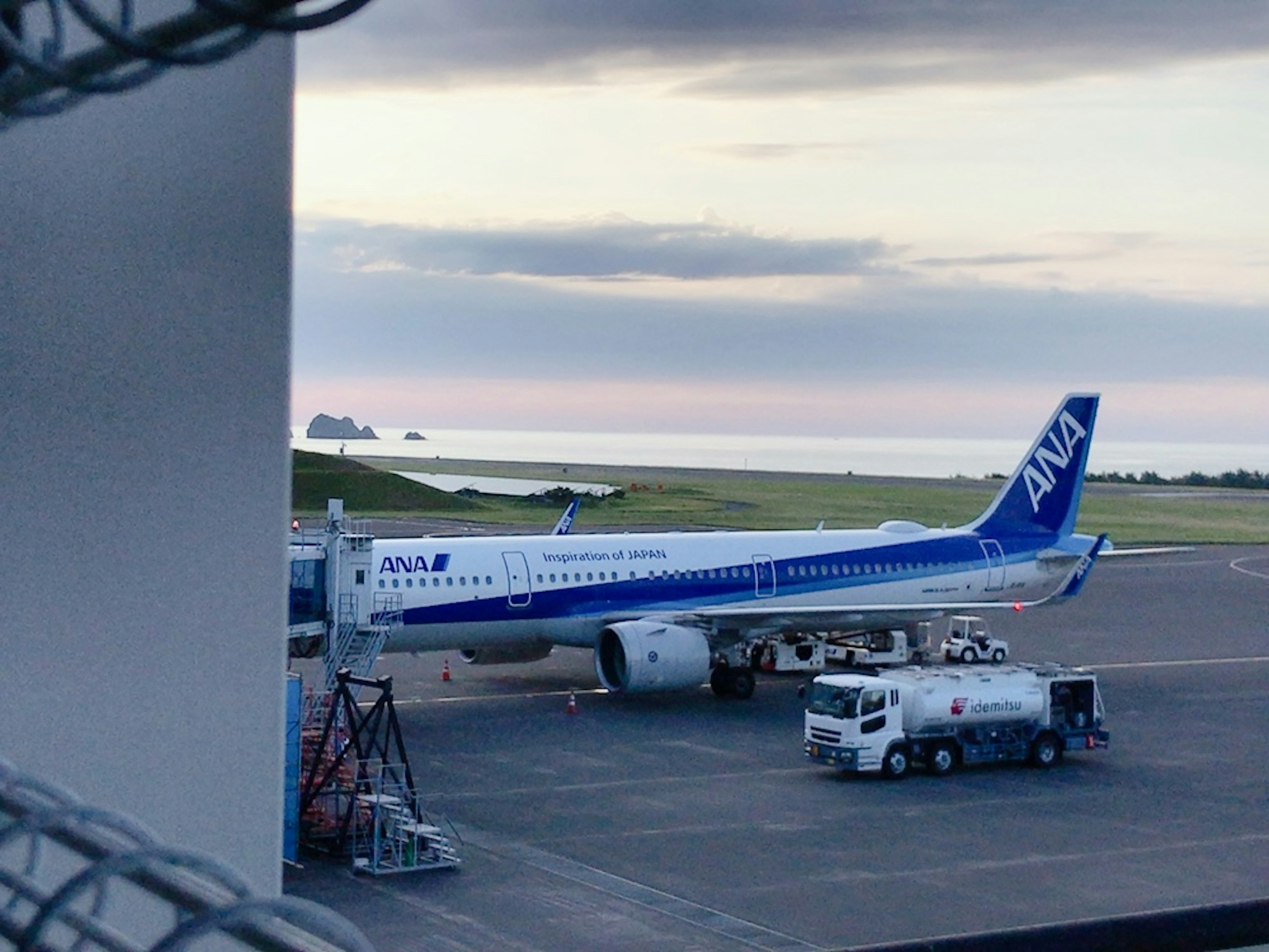 ANA客機停在機場，背景有海洋和雲朵