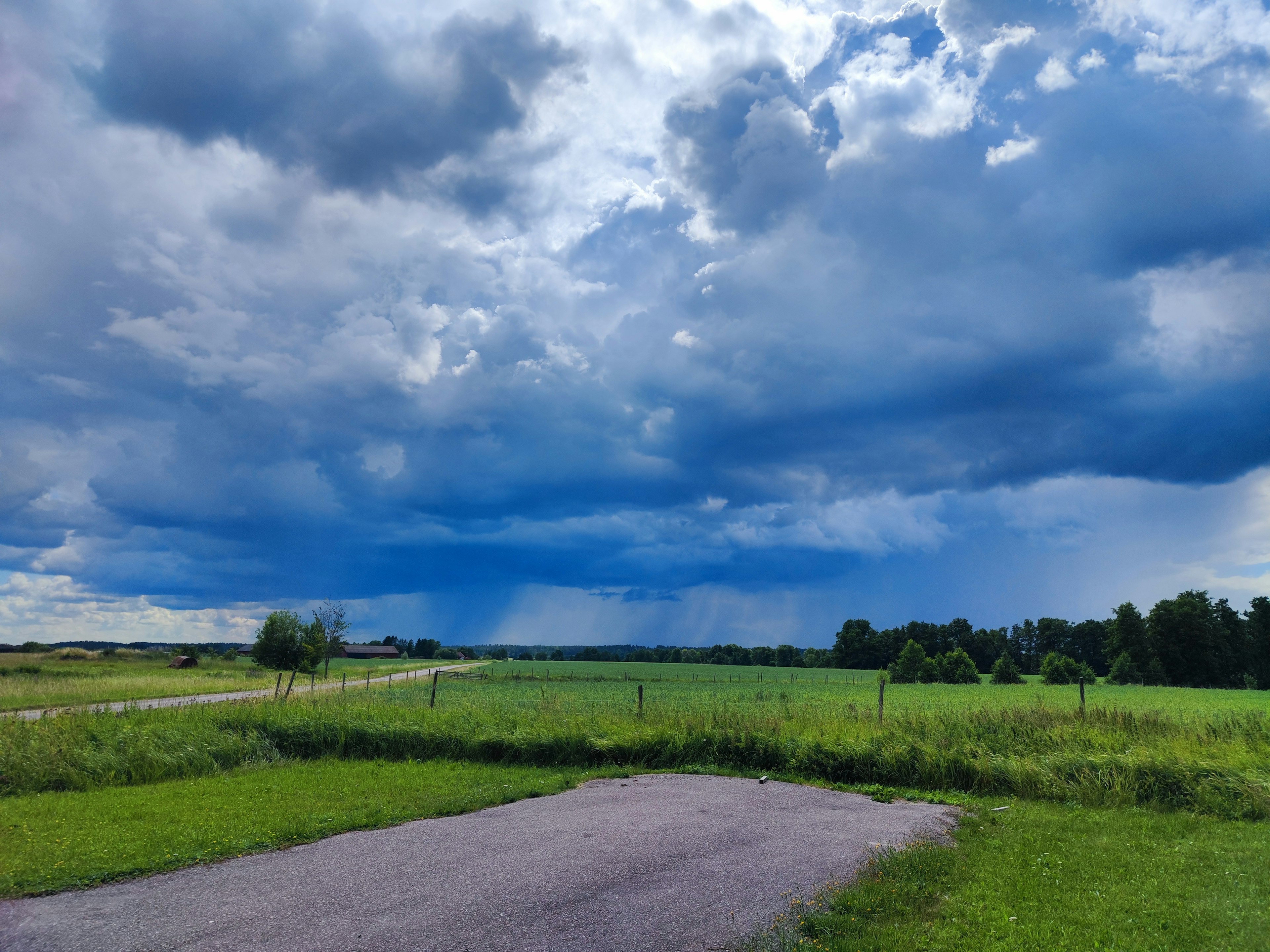 Landscape with dark clouds and blue sky green grass field and paved road