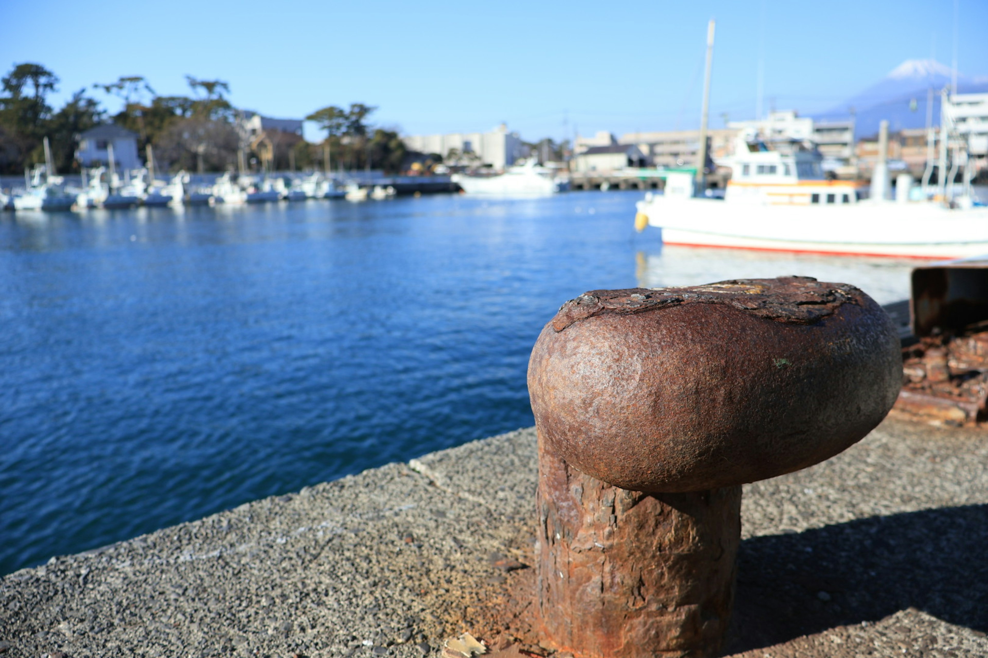 Ancien poteau d'amarrage en fer au bord du port avec de l'eau calme et des bateaux en arrière-plan