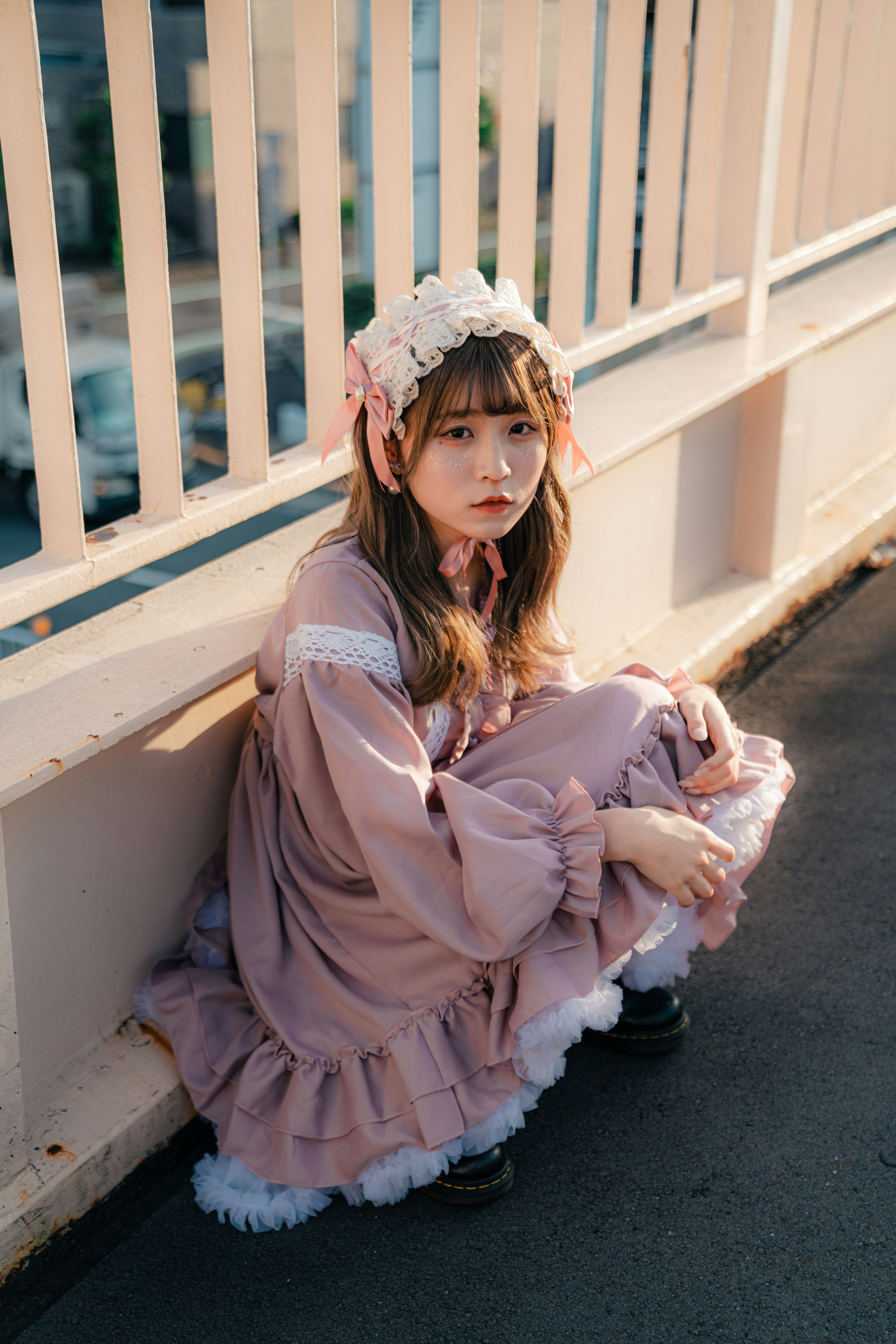 A girl in a light pink dress sitting against a wall