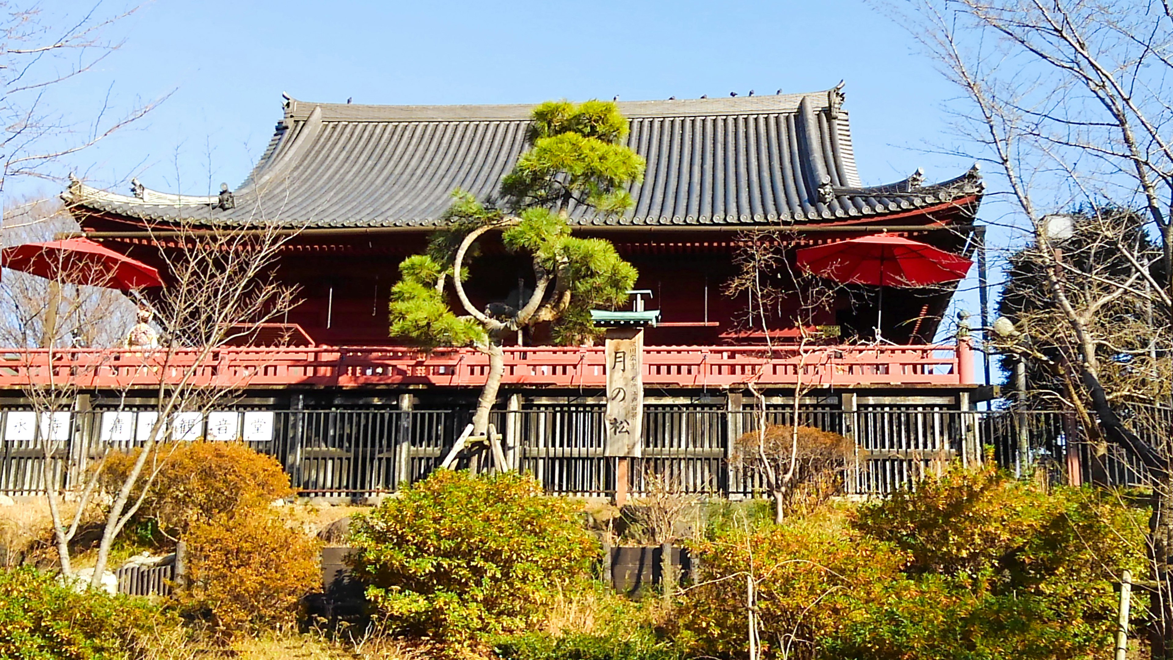 Traditionelles japanisches Gebäude mit roten Geländern und Ziegeldach umgeben von grünen Bäumen und Garten