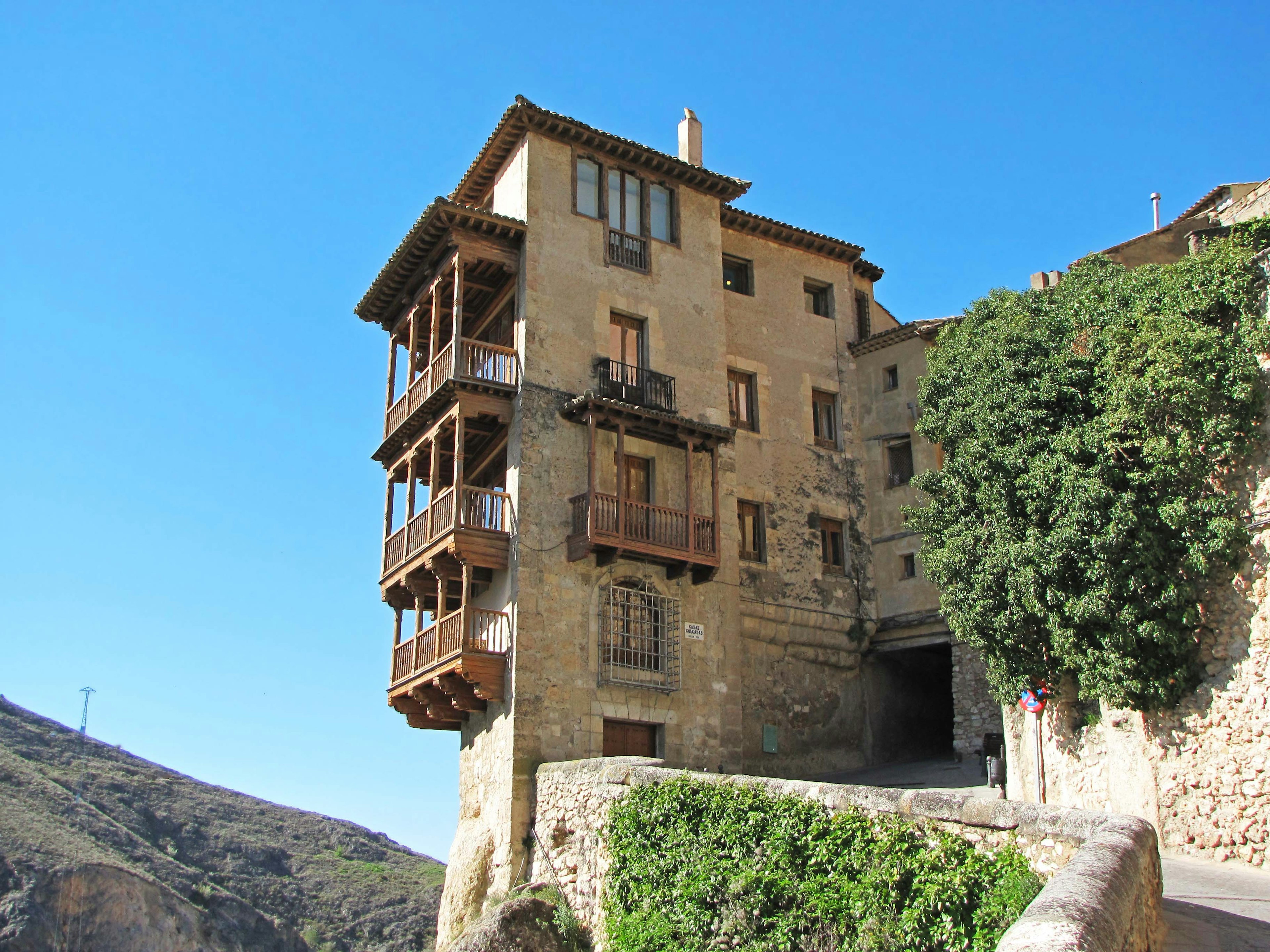 Unique building perched on a cliff surrounded by greenery under a blue sky